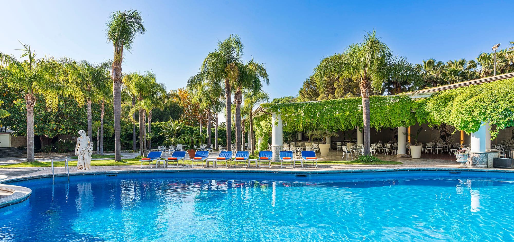 Swimming pool and outdoor seating area with palm trees and a statue.