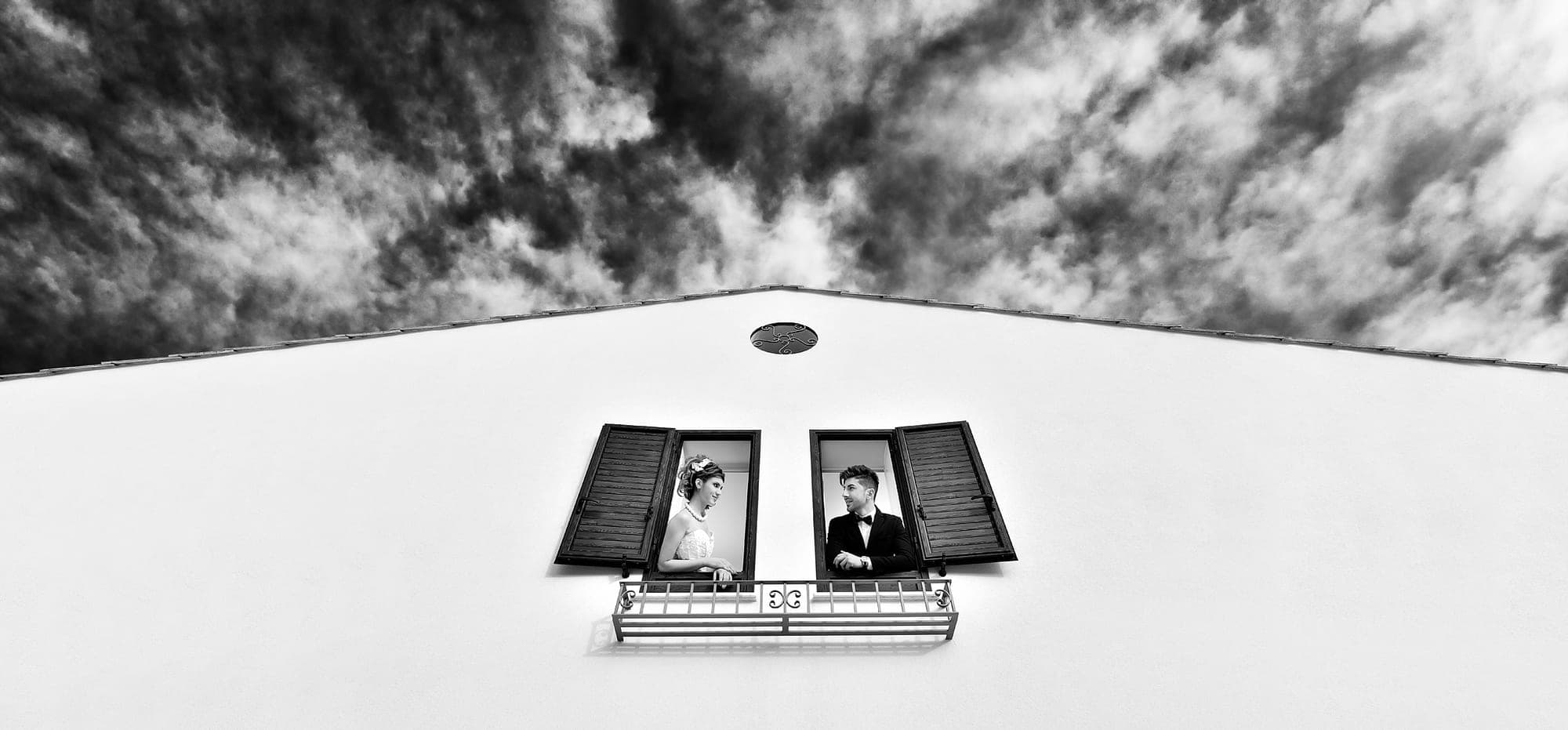 Bride and groom in windows of a building with a dramatic sky