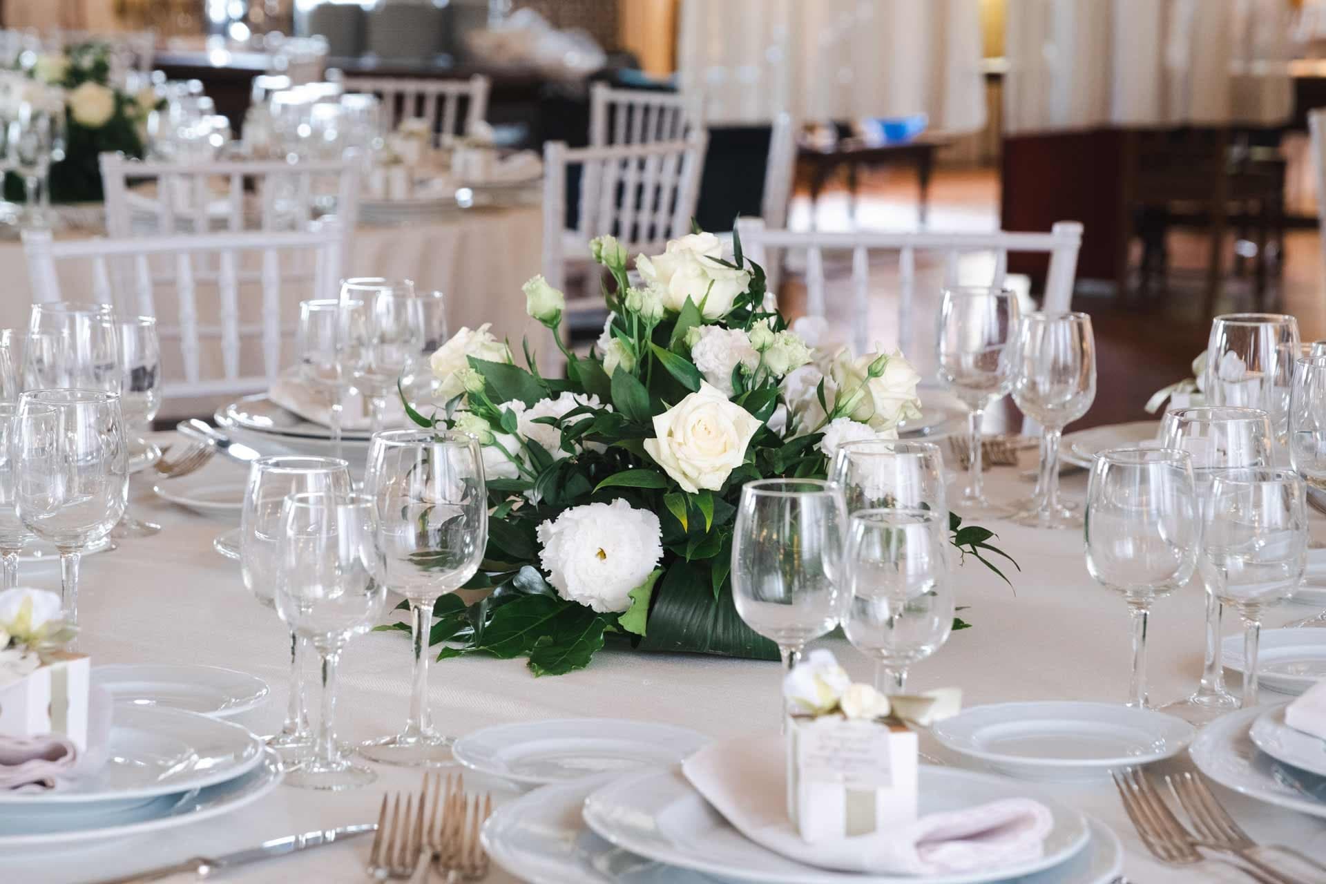 A wedding reception table setting with white roses and place settings.