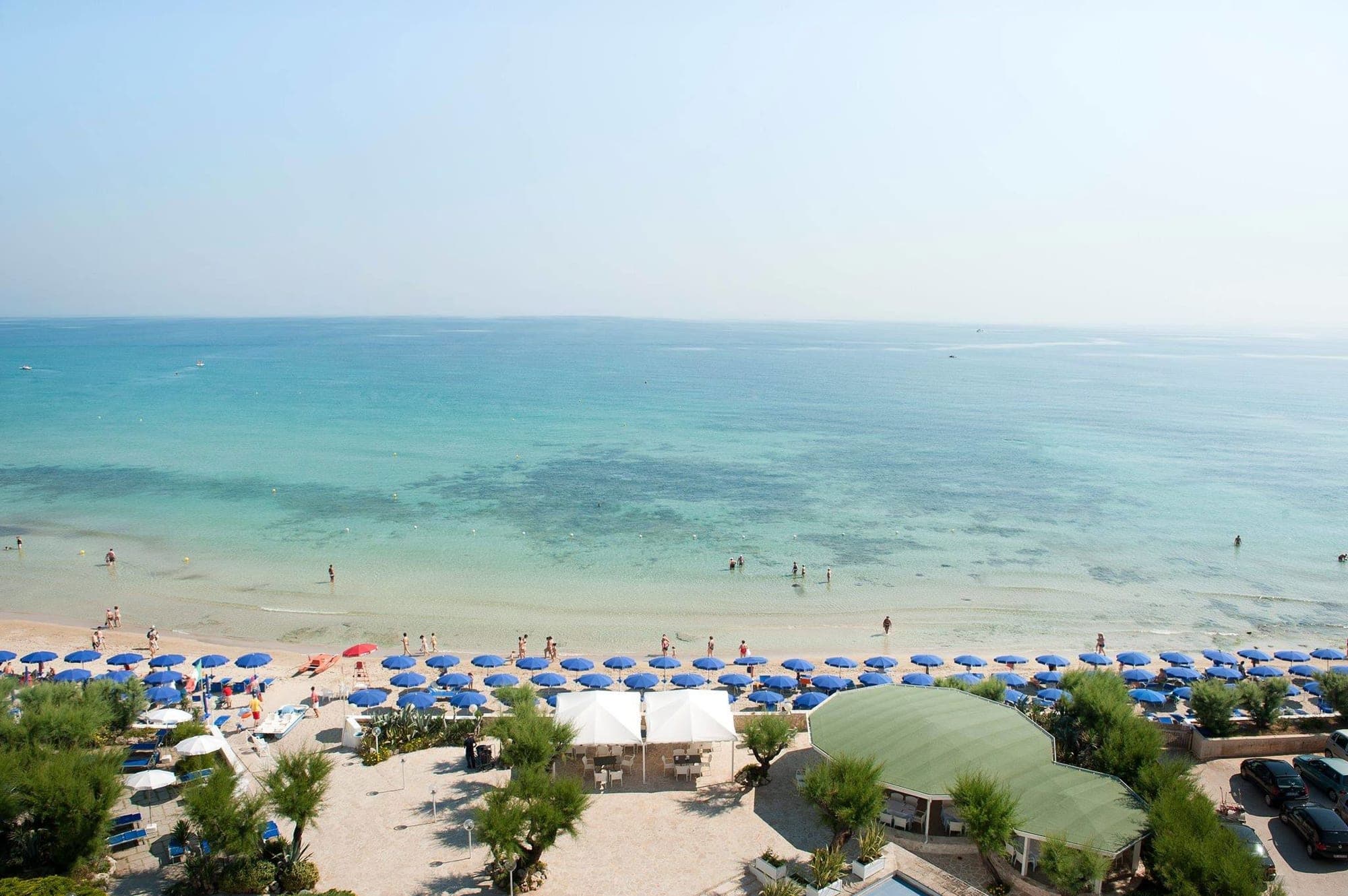 A beach with blue umbrellas and people by the turquoise sea.