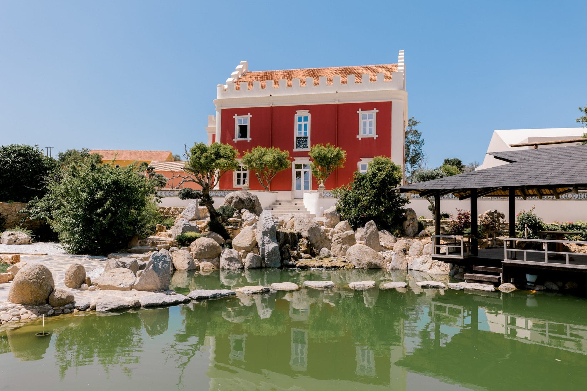 Red building with a pond and a gazebo on a sunny day.