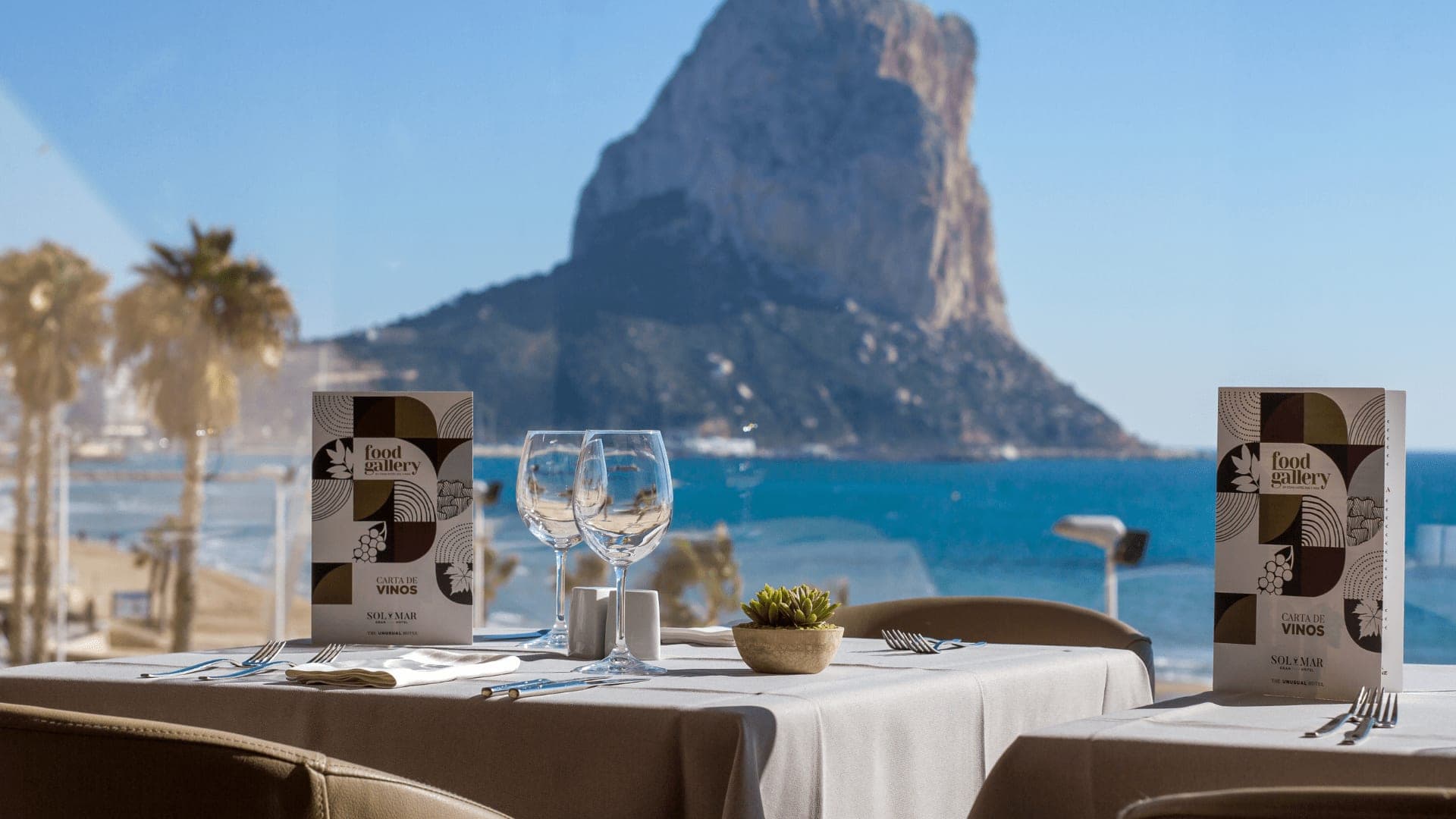 A table set for dining with a view of the sea and a large rock formation.