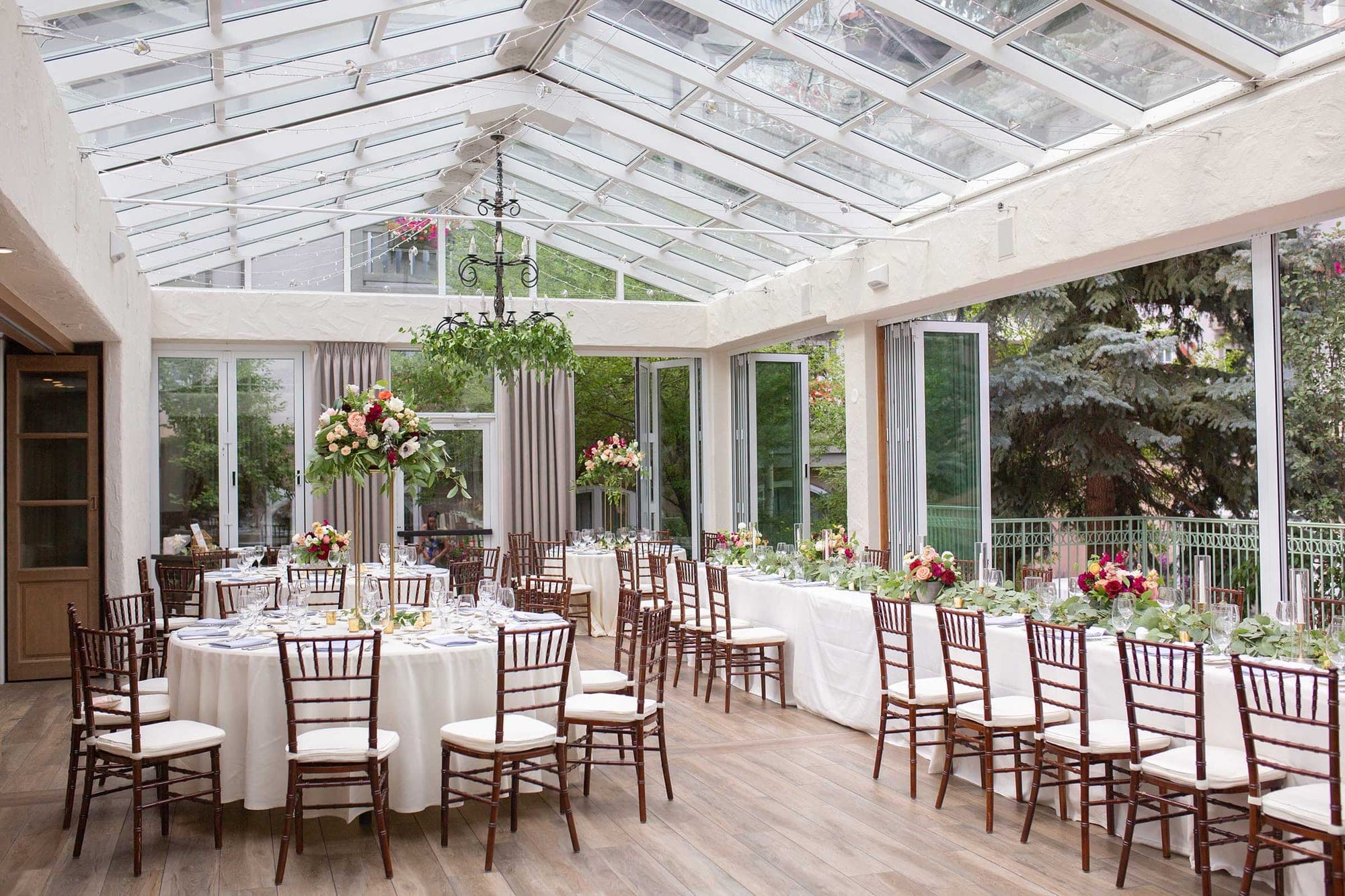 A reception room with round and long tables set for a wedding, featuring floral centerpieces and chairs.