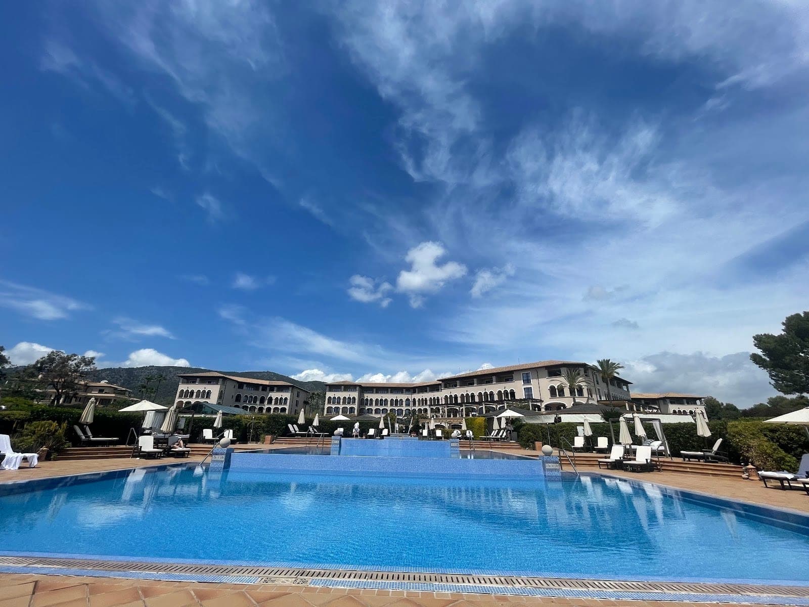 A large blue swimming pool with lounge chairs and umbrellas in front of a hotel building.