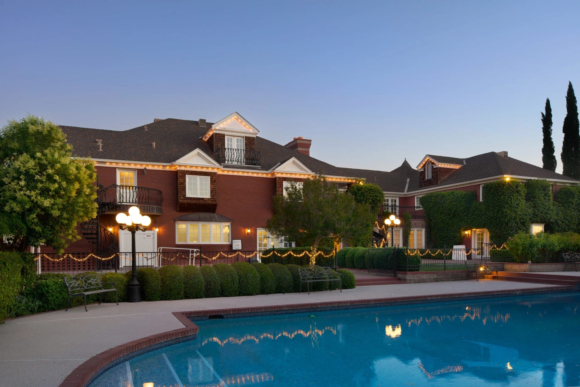 Exterior of a red building with a pool in the foreground at dusk.