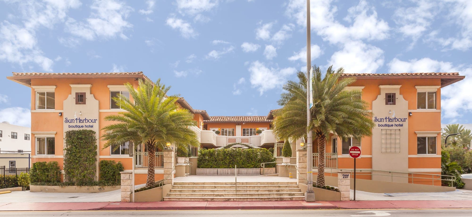 Exterior of Sun Harbour Boutique Hotel with palm trees and a wide staircase.