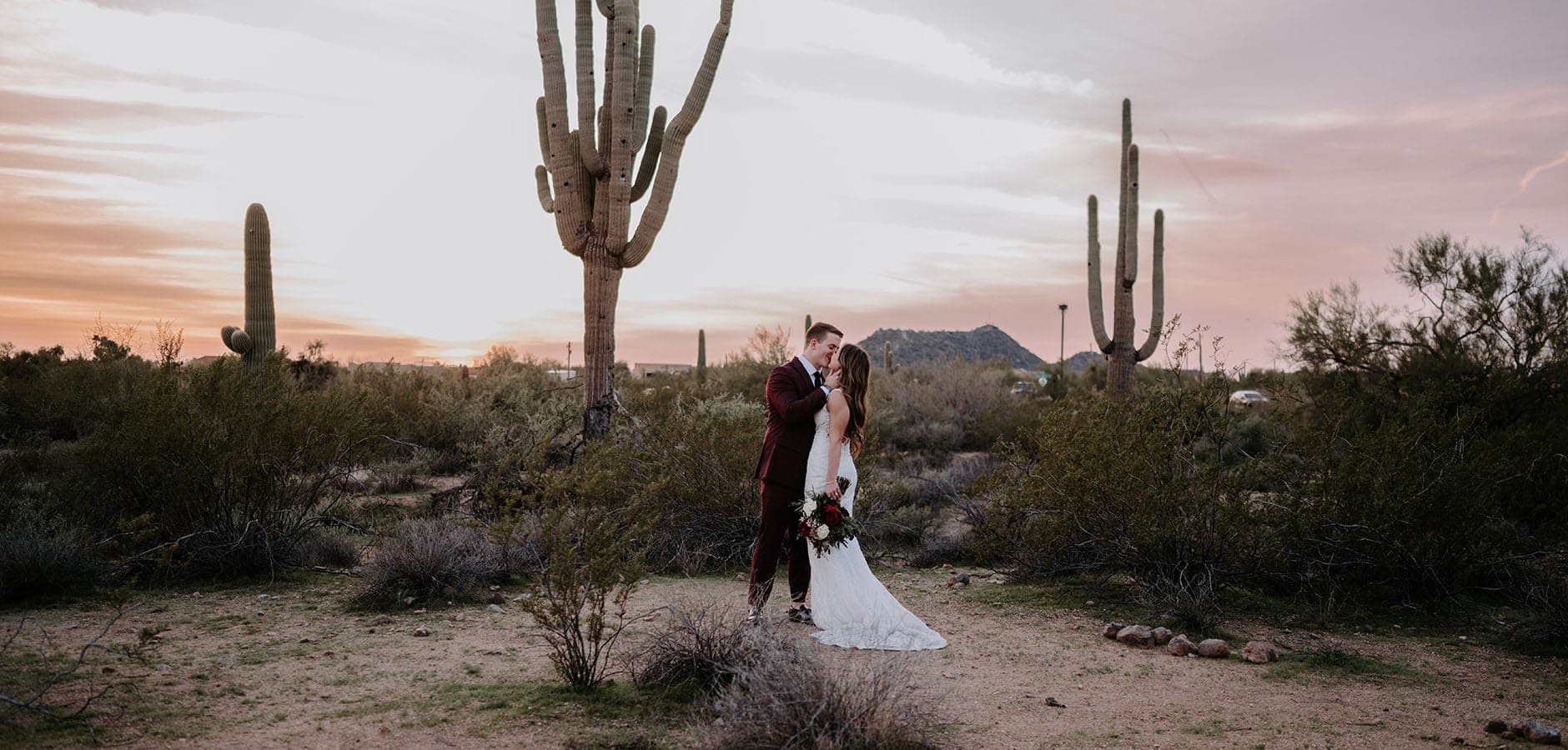 Couple kissing in desert with saguaro cacti at sunset