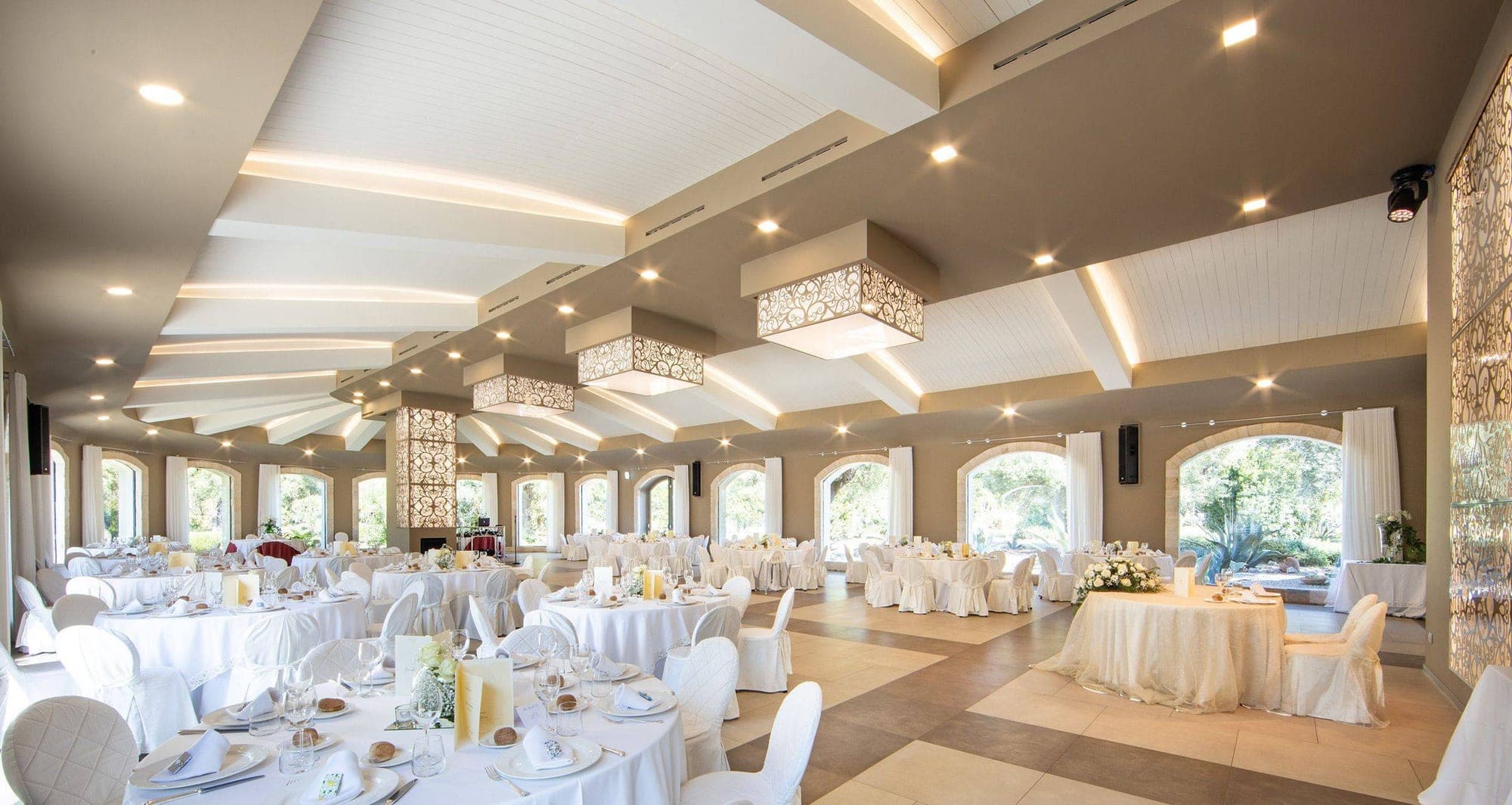 A wedding reception hall with many tables set for guests.