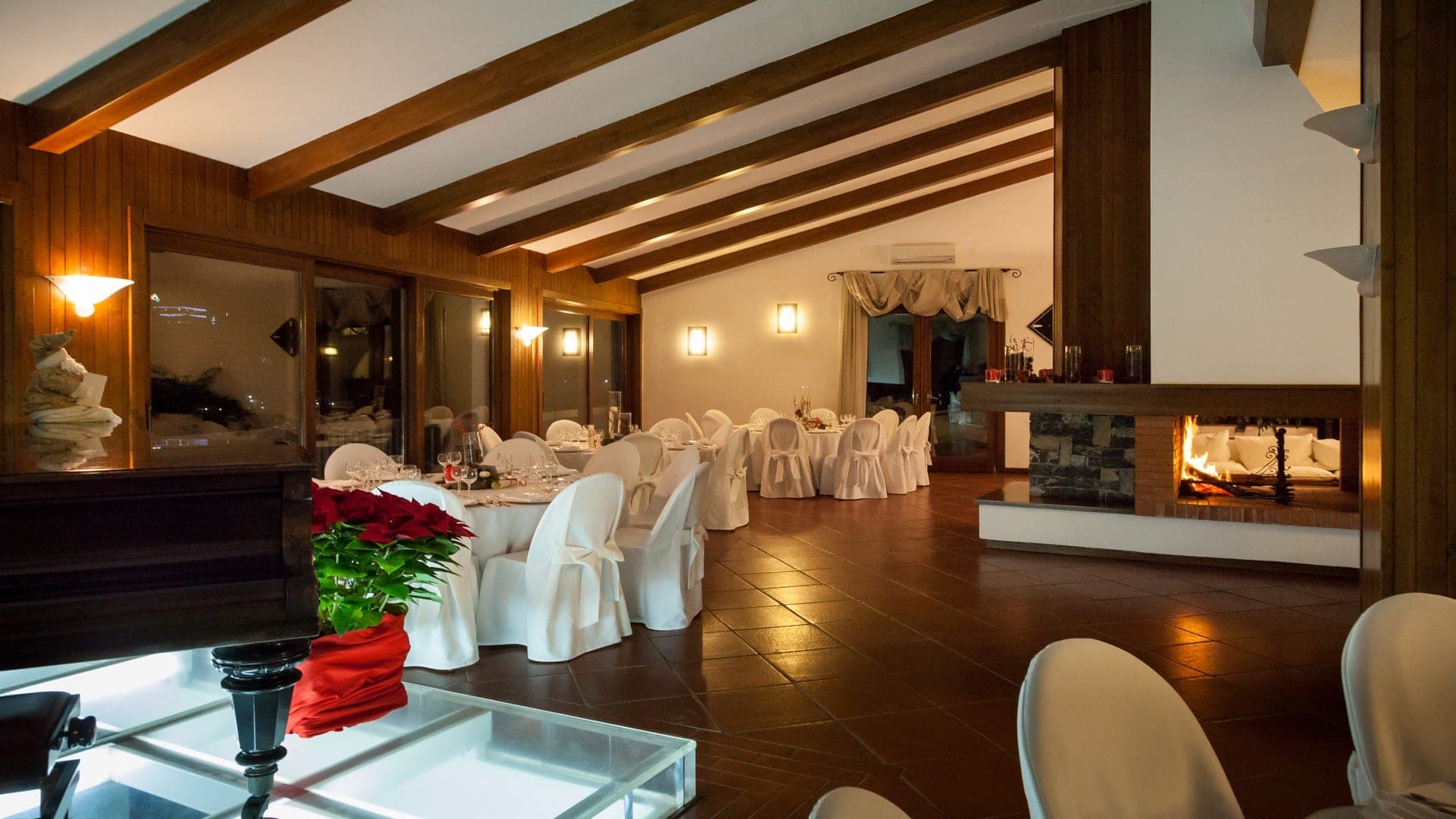 A reception room with tables set for a wedding and a fireplace.
