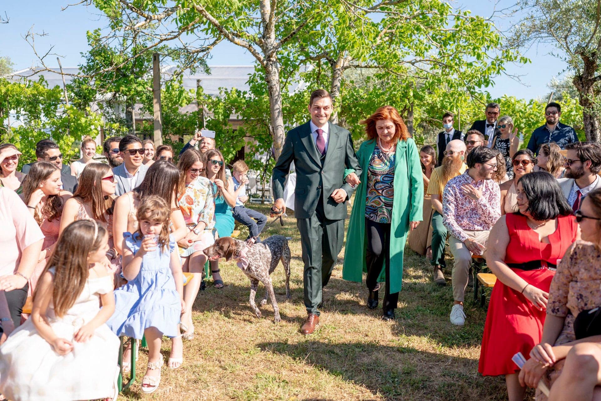 A wedding party walks down an aisle with guests seated on either side.