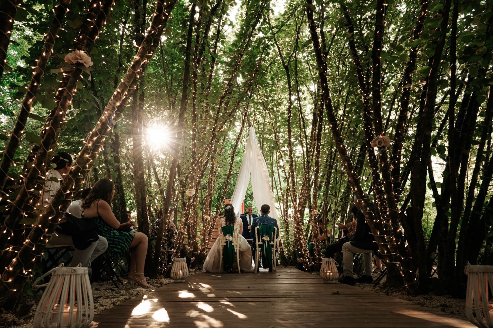 Wedding ceremony in a forest with trees wrapped in fairy lights.