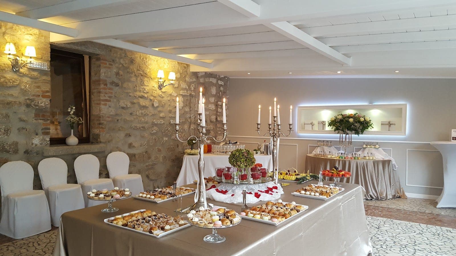 Dessert buffet with pastries and fruit in a room with stone walls and white chairs.