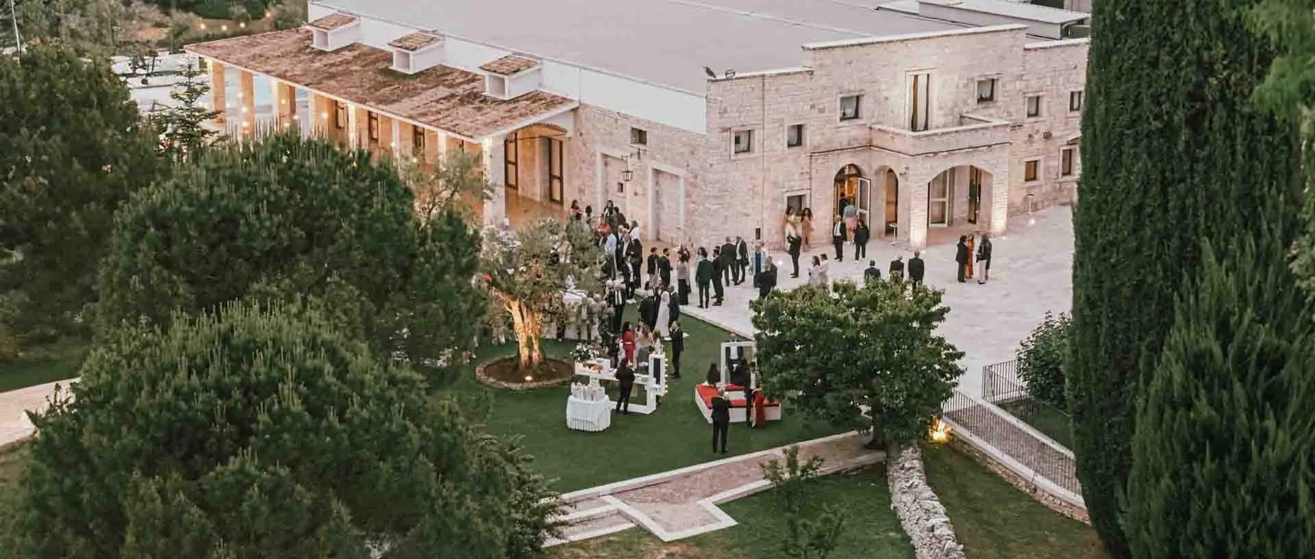 Wedding reception in the courtyard of a stone building with guests and trees.