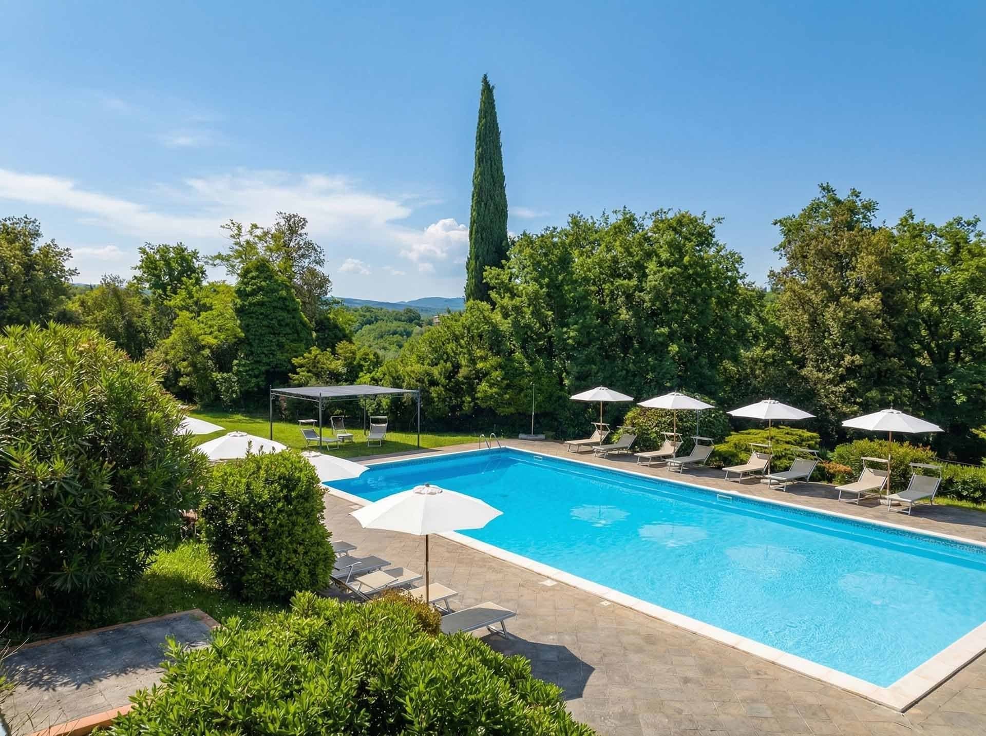 A swimming pool with lounge chairs and umbrellas surrounded by trees and greenery.