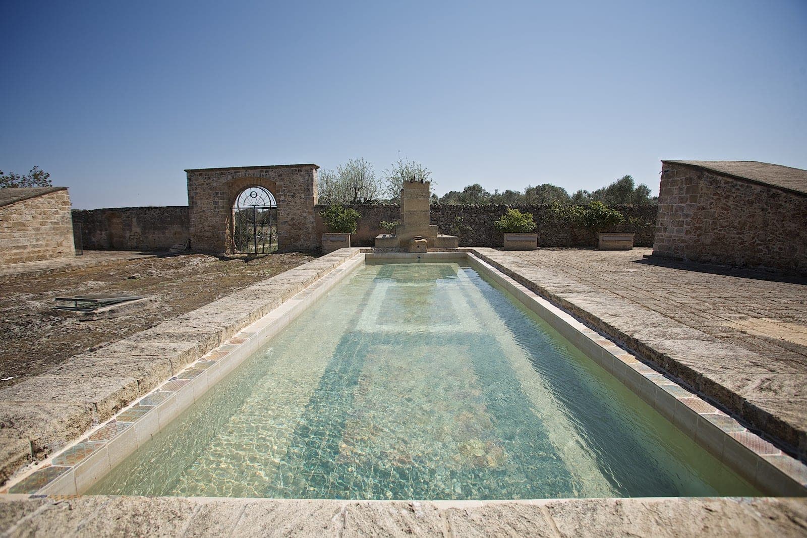 A long, narrow pool with stone surrounds and a clear blue sky.