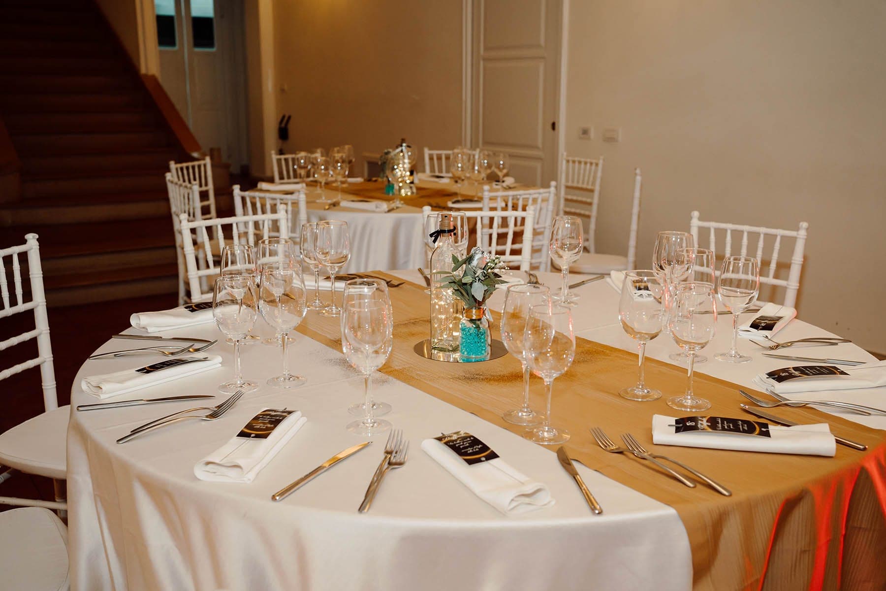 A round reception table is set with white linens, place settings, and glassware.