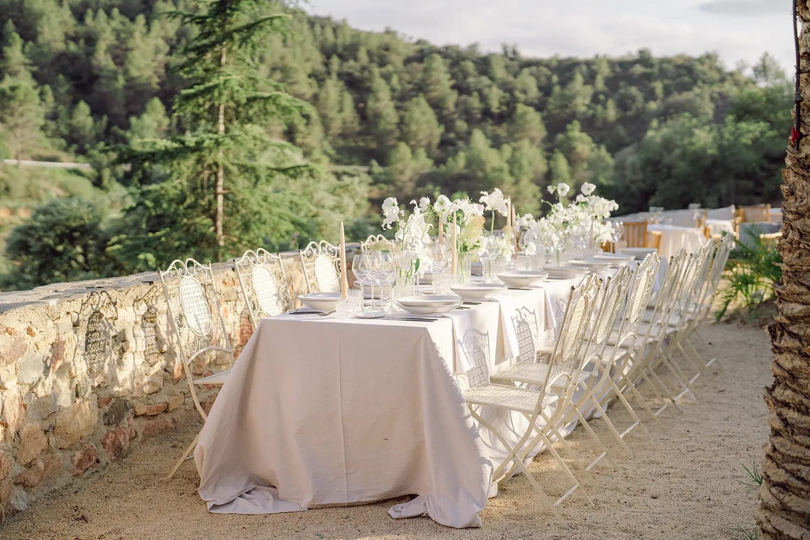 Outdoor reception table setting with white chairs and floral arrangements.