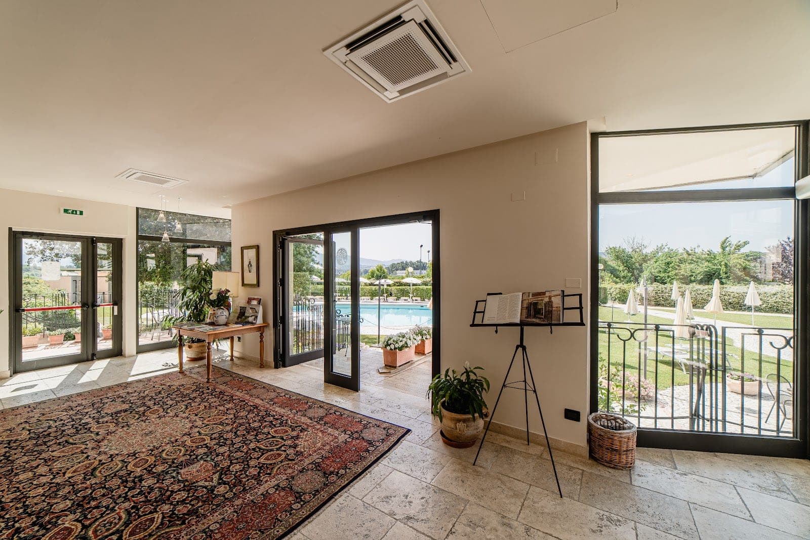 Interior hallway with a large rug, leading to glass doors with a view of a swimming pool and garden.