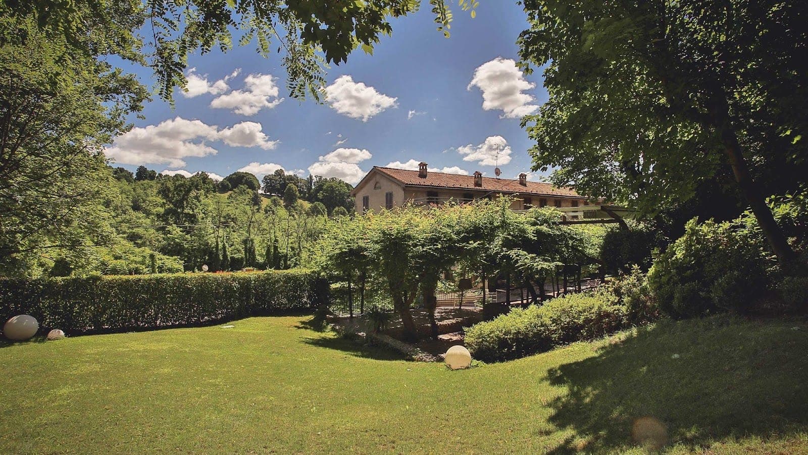 A green lawn with trees and a building in the background under a blue sky with clouds.