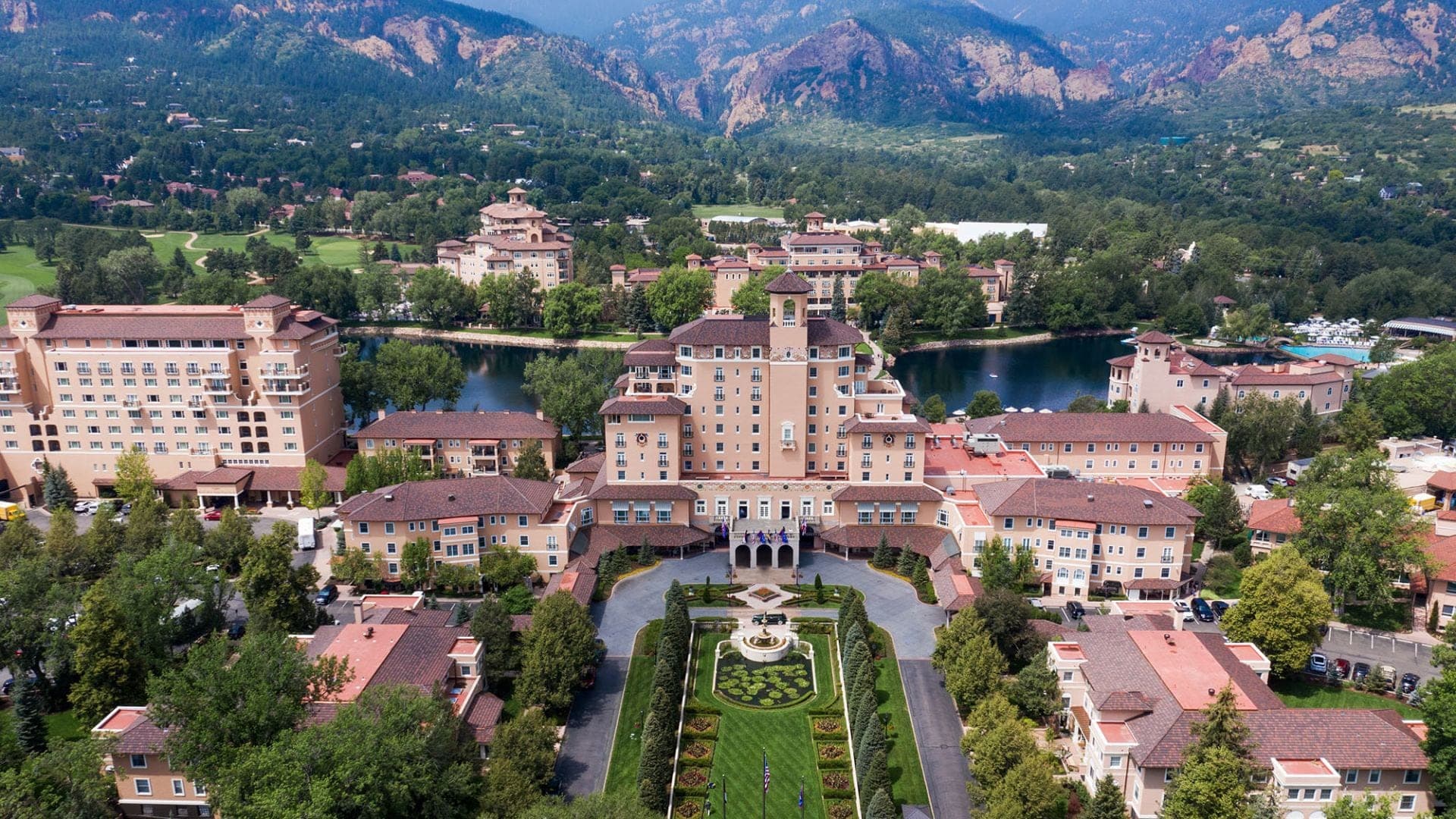 Aerial view of a large hotel complex with a lake and mountains in the background.