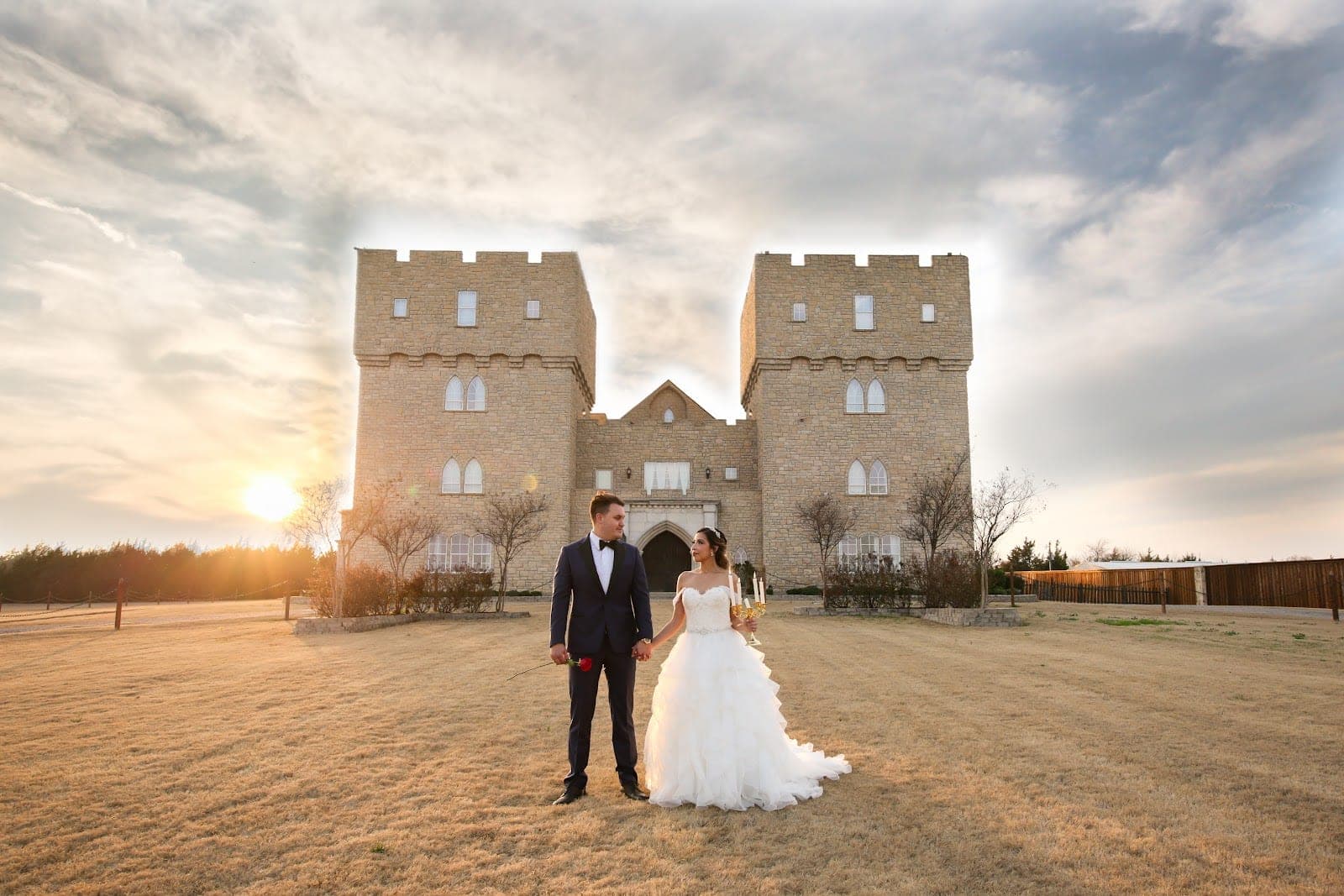 A bride and groom stand in front of a castle at sunset.