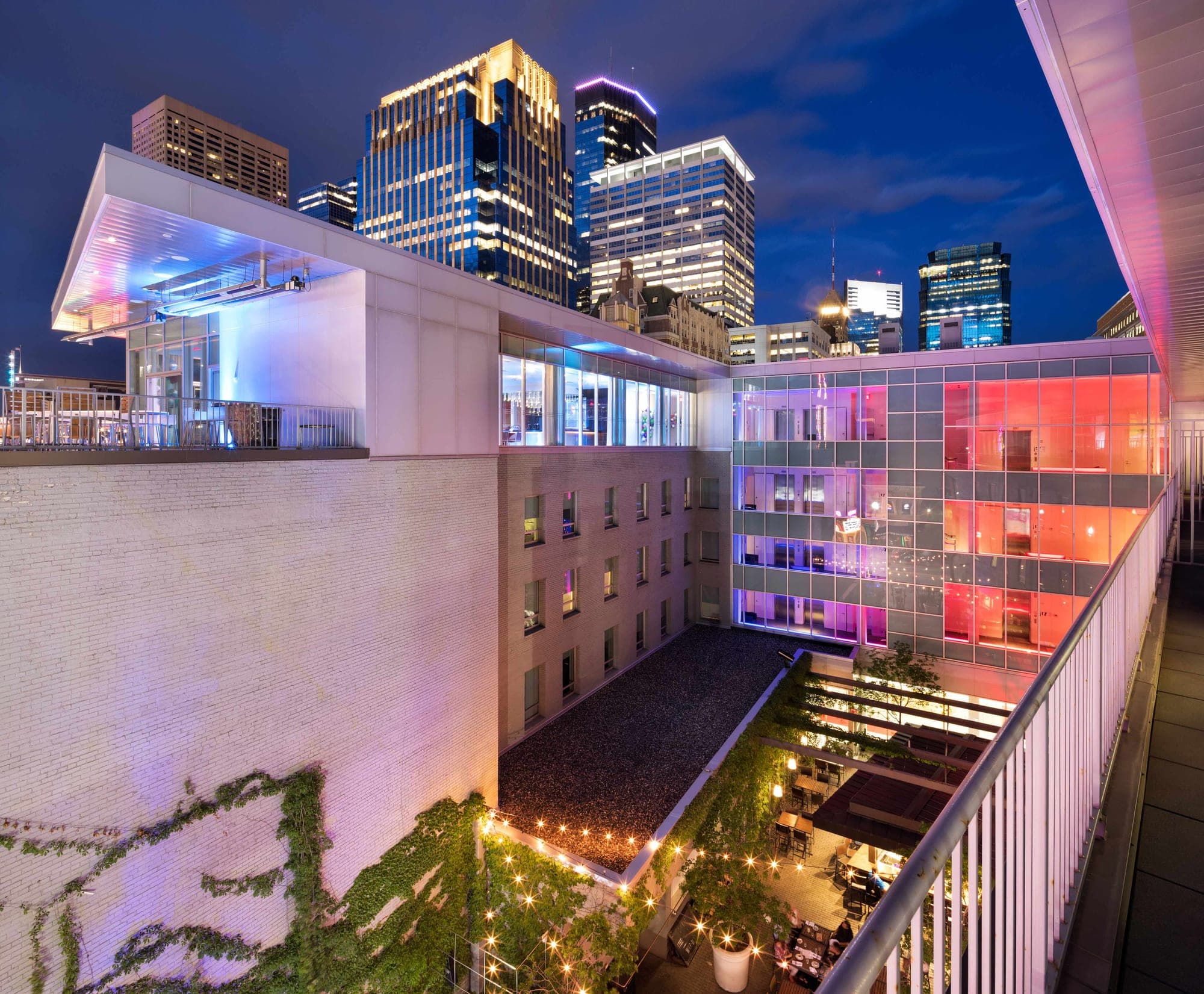 Rooftop terrace and courtyard of a hotel at dusk with city skyline