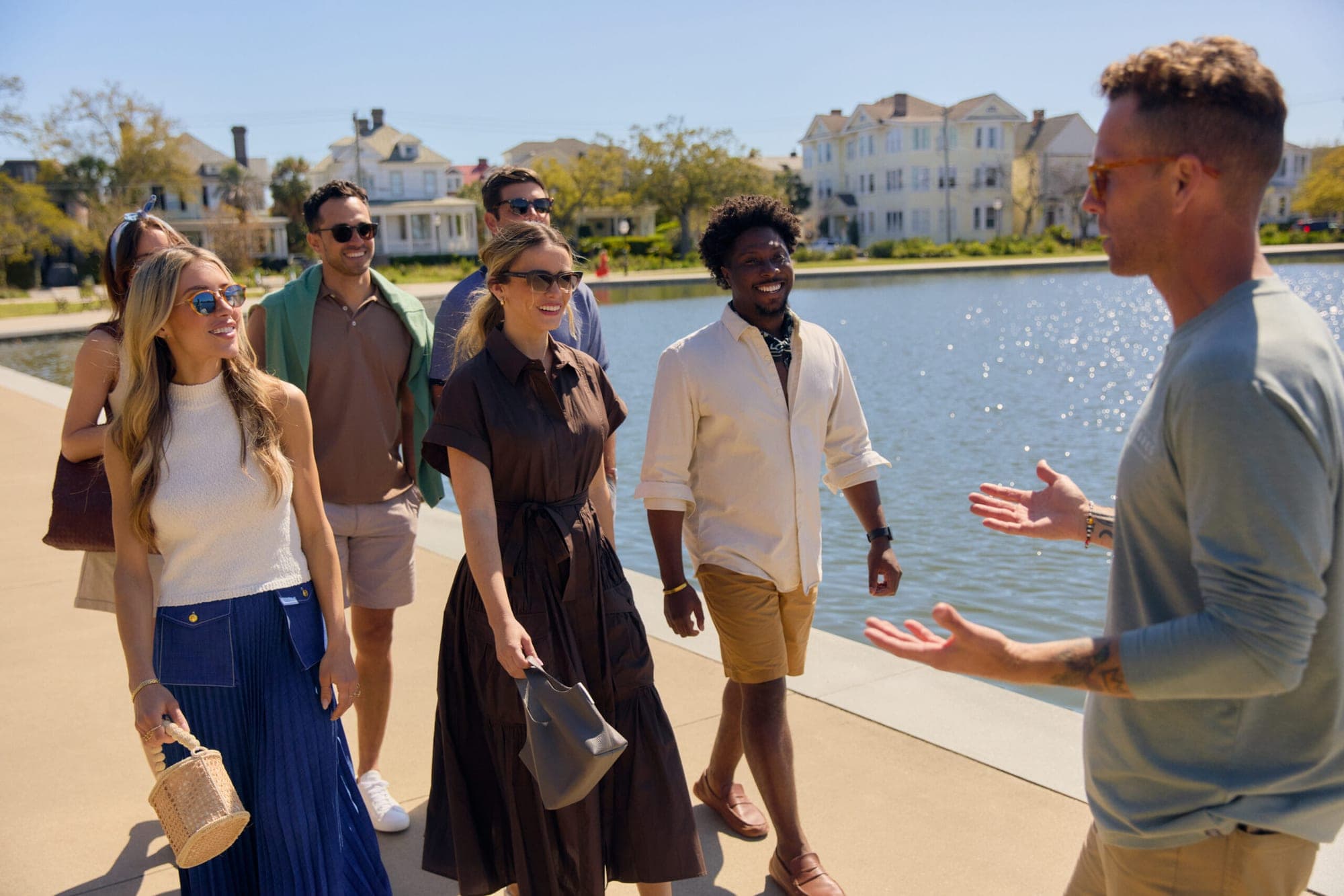 A group of people walk along a waterfront path with buildings in the background.