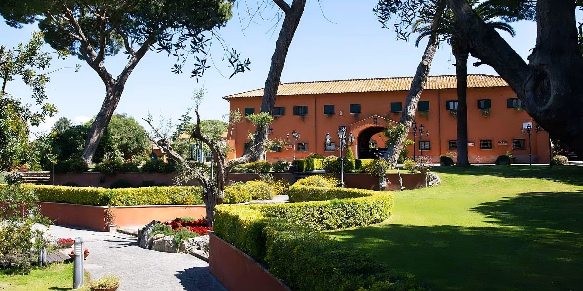 Exterior of an orange building with a terracotta roof, surrounded by green lawns and trees.