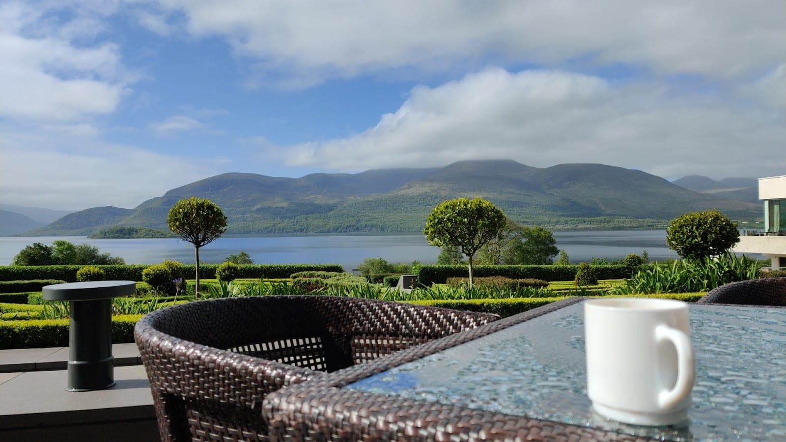 View of a lake and mountains from a terrace with a cup of coffee.