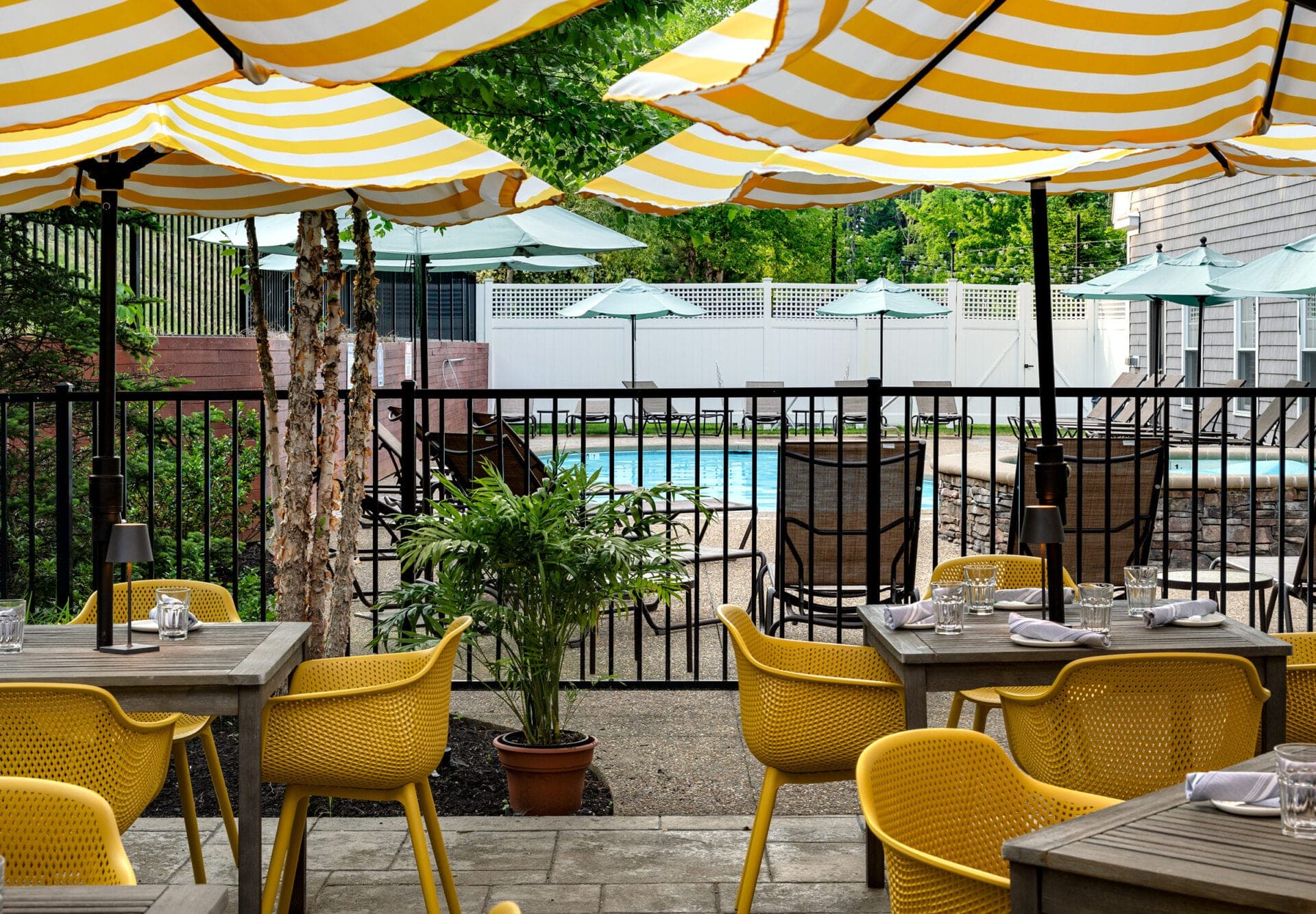 Outdoor seating area with yellow chairs and tables by a swimming pool.