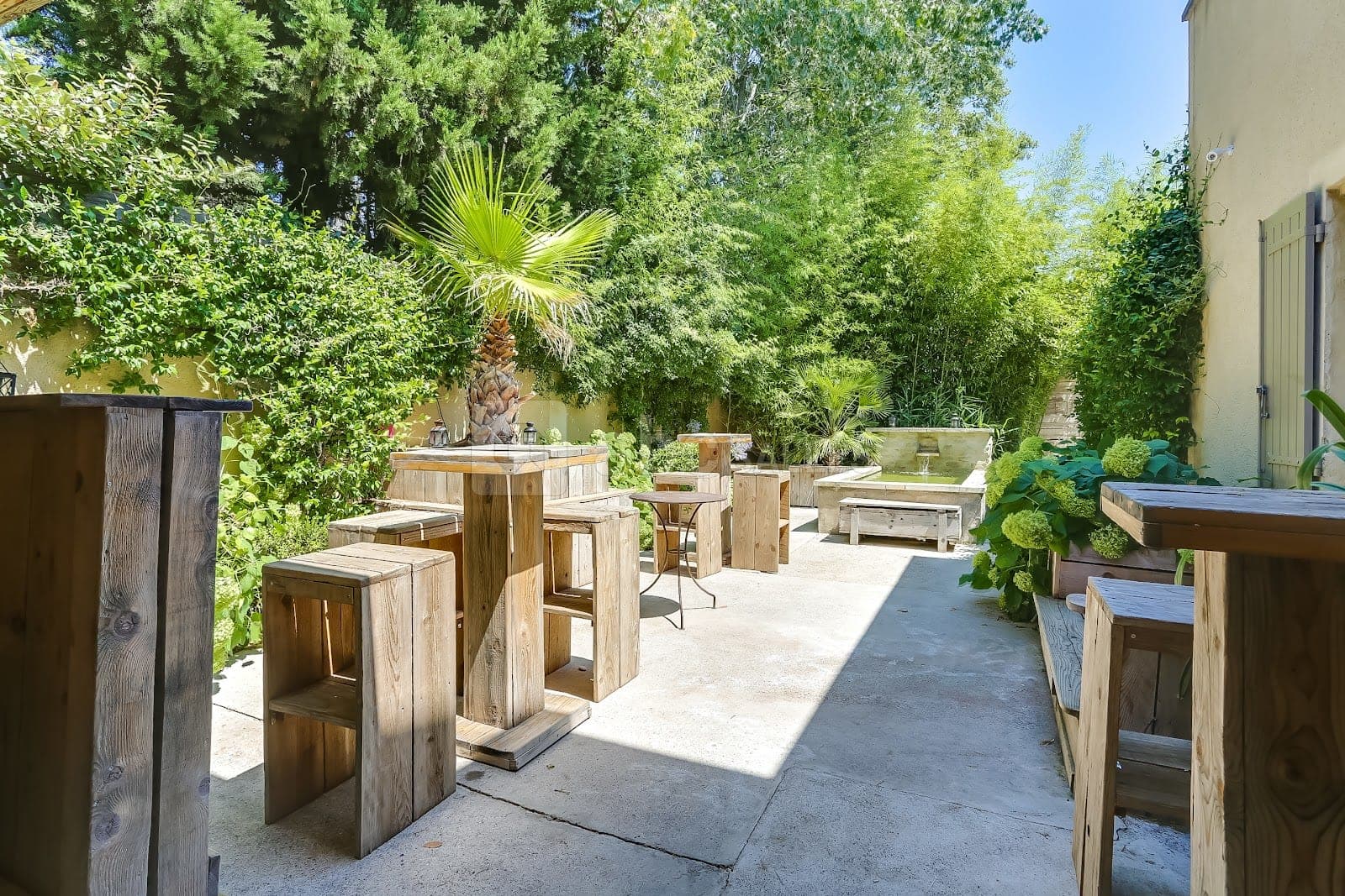 Outdoor seating area with wooden tables, stools, and a water feature.