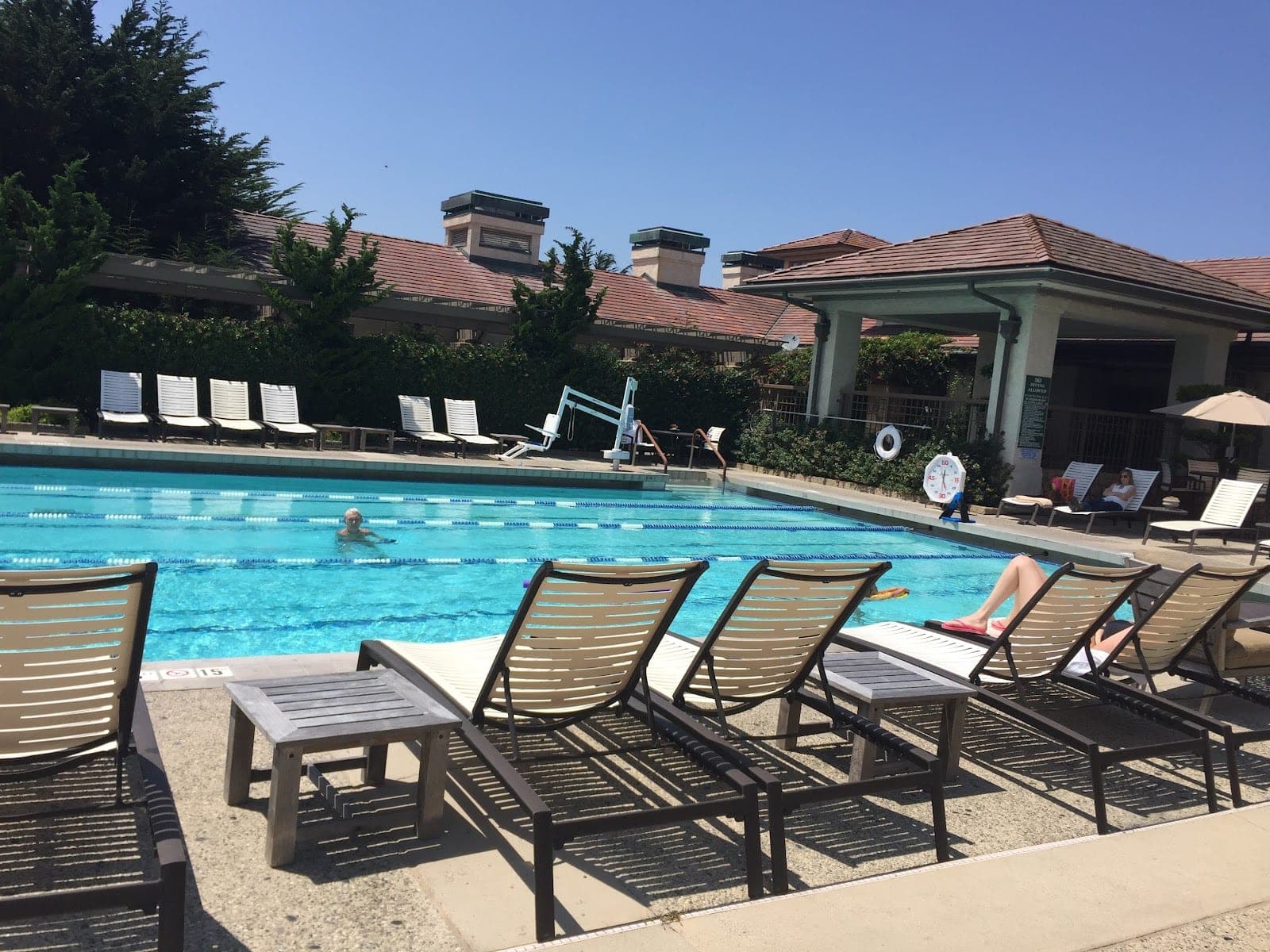 Swimming pool with lounge chairs and people relaxing under a clear blue sky.