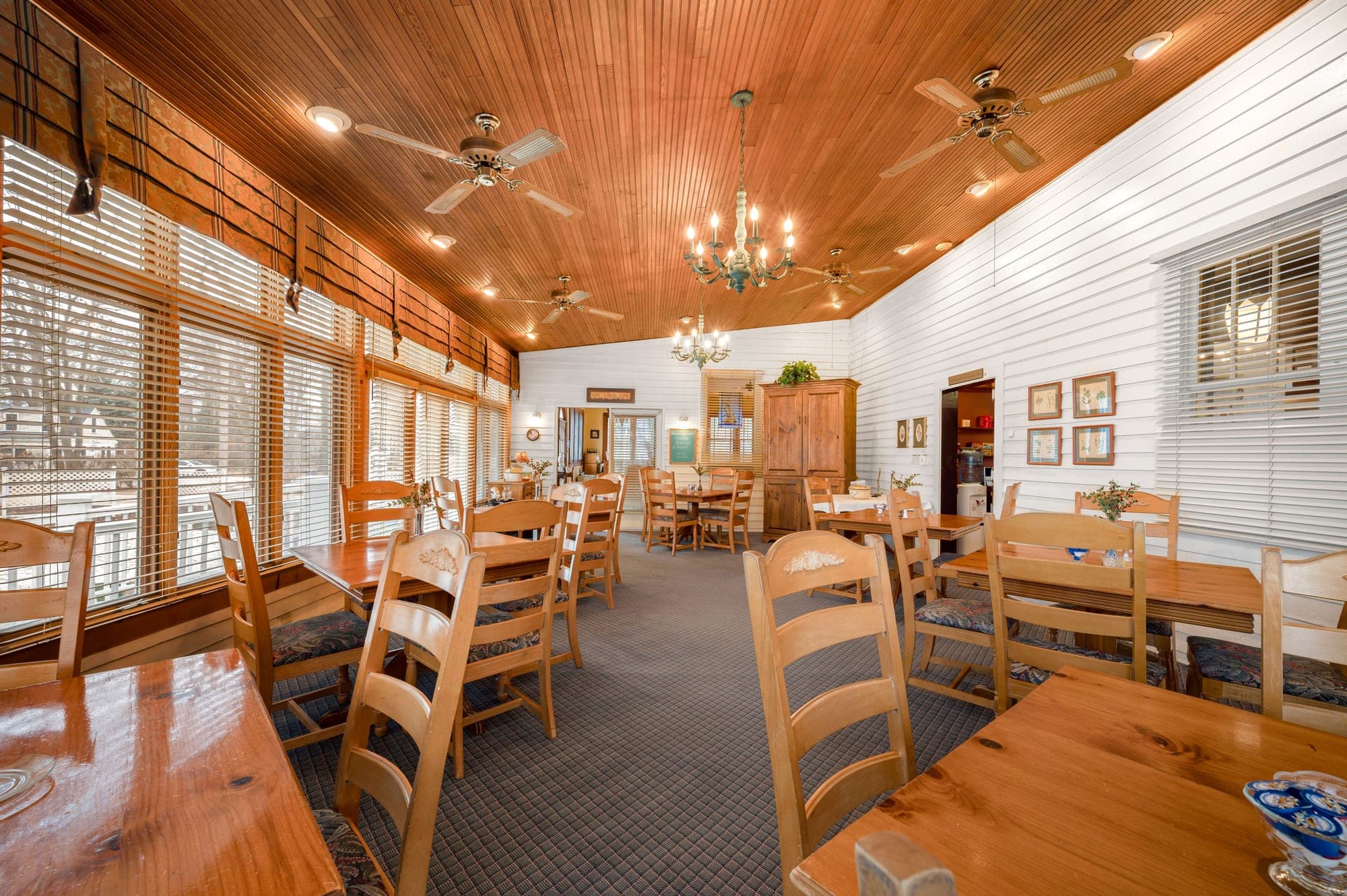 Dining room with wooden tables and chairs, and large windows.