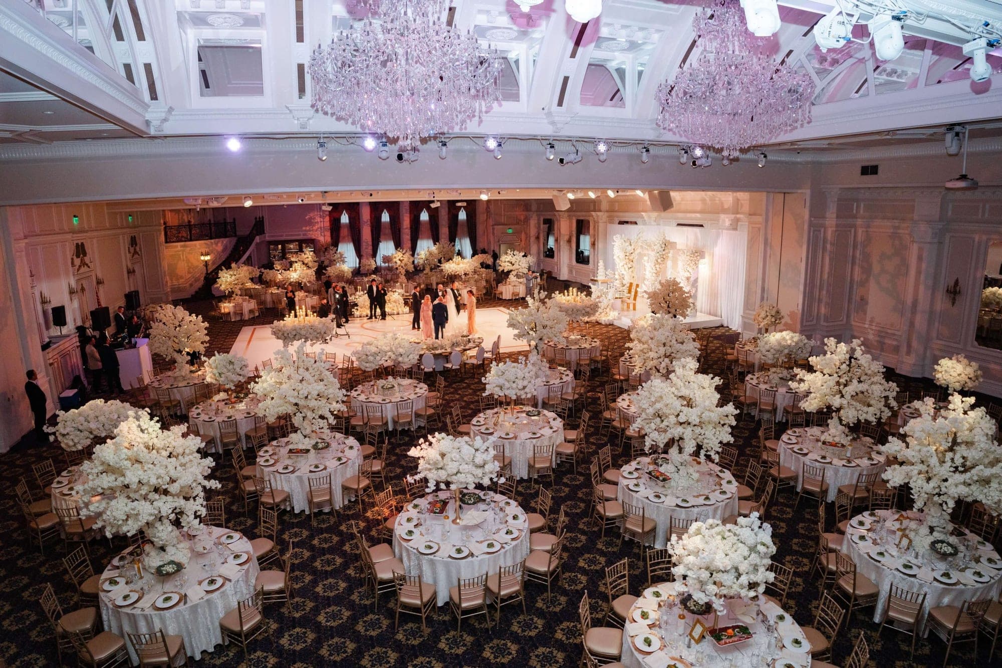 A large ballroom decorated for a wedding reception with round tables and floral centerpieces.