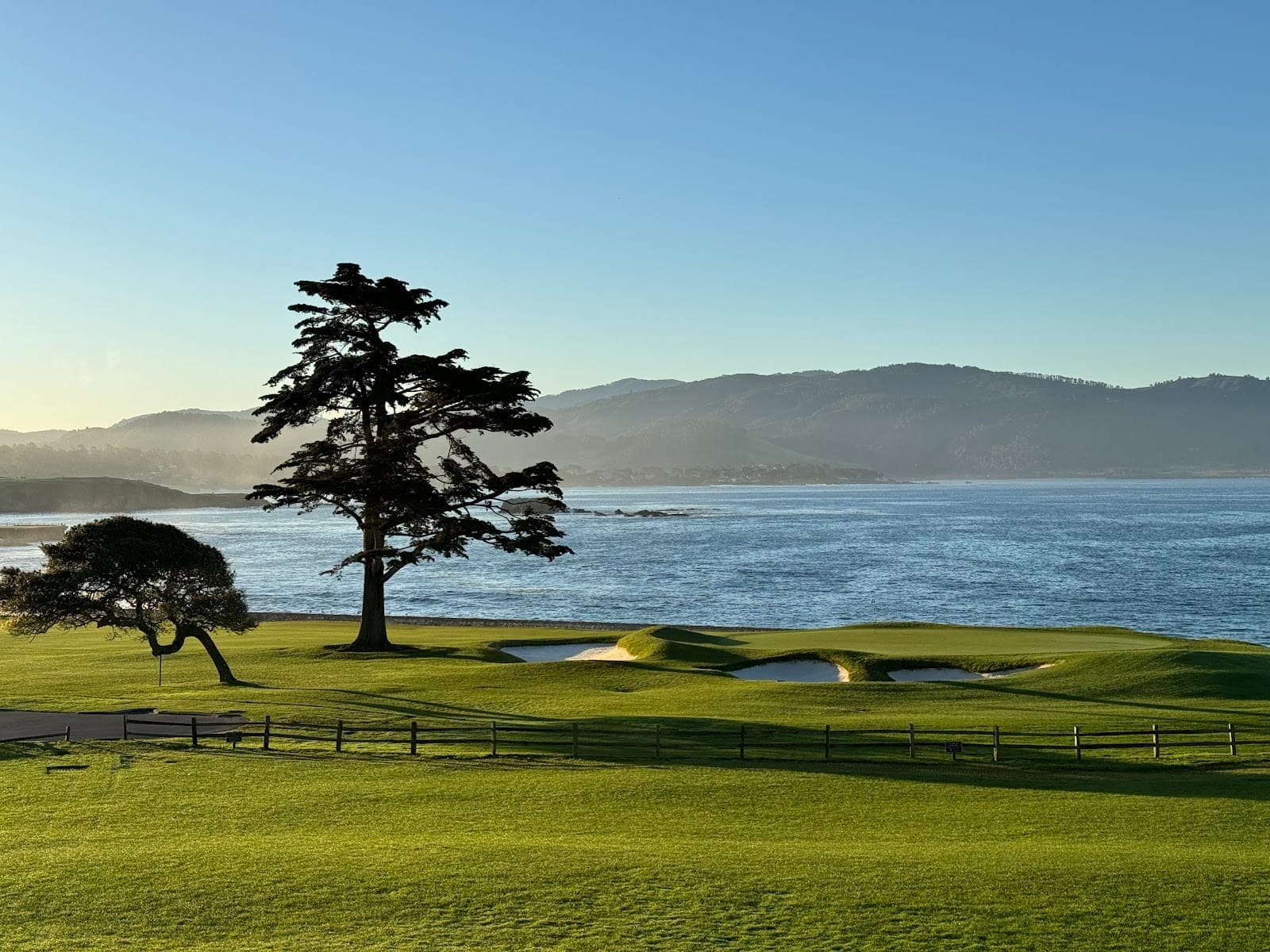 A golf course with trees and a view of the ocean and hills.