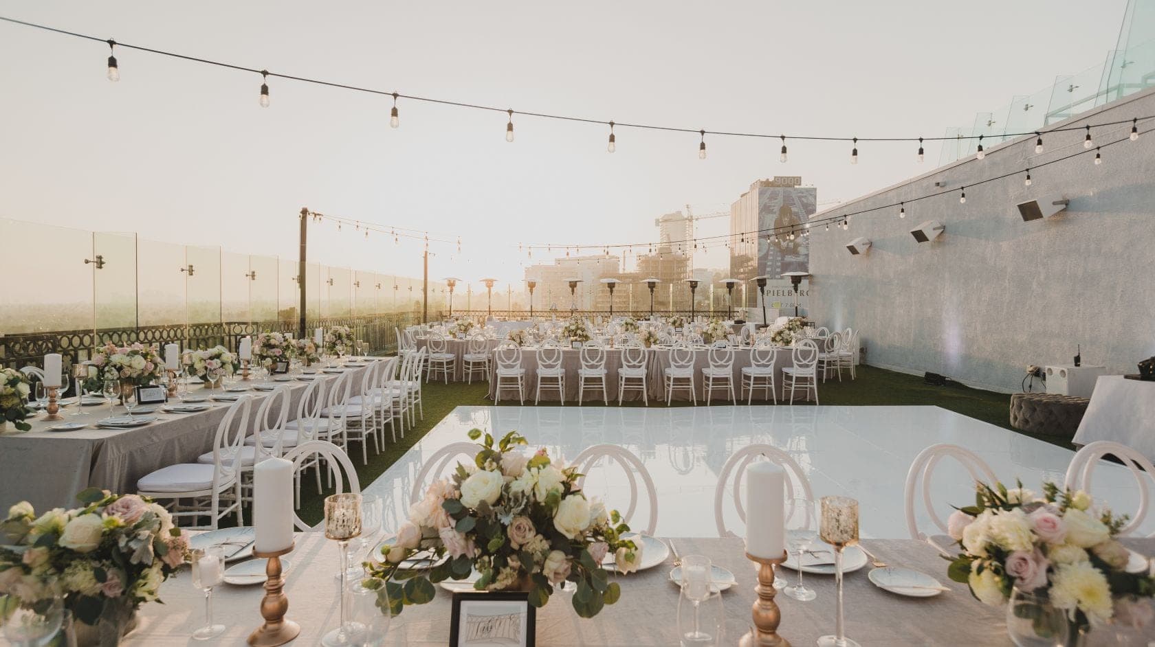 Rooftop reception area with tables, chairs, and string lights.