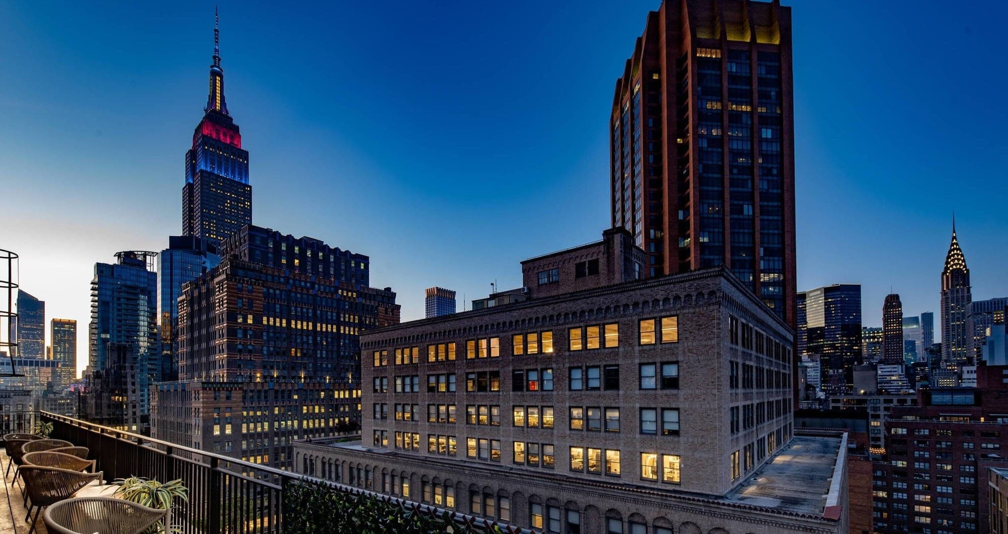 Rooftop terrace overlooking the New York City skyline at dusk, with the Empire State Building visible.