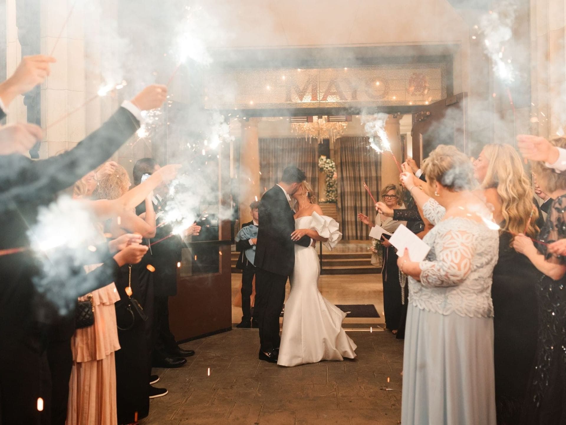 Wedding couple kissing with sparklers and guests celebrating