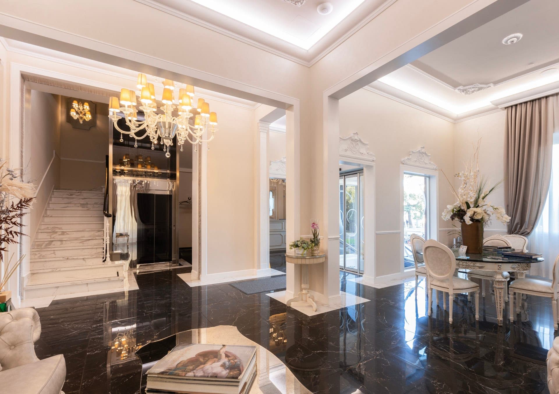 Interior of a hotel lobby with a grand chandelier, marble staircase, and dining area.