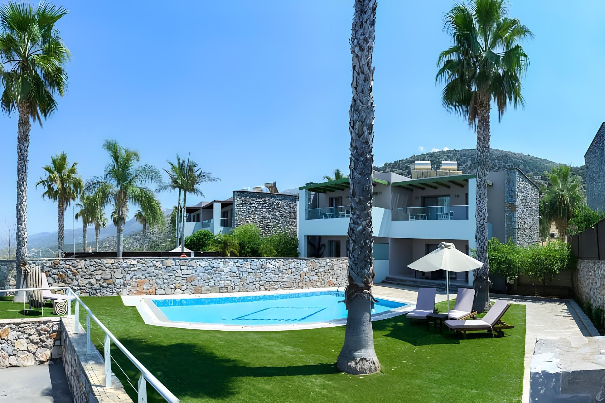 Resort grounds with a swimming pool, lounge chairs, palm trees, and buildings.