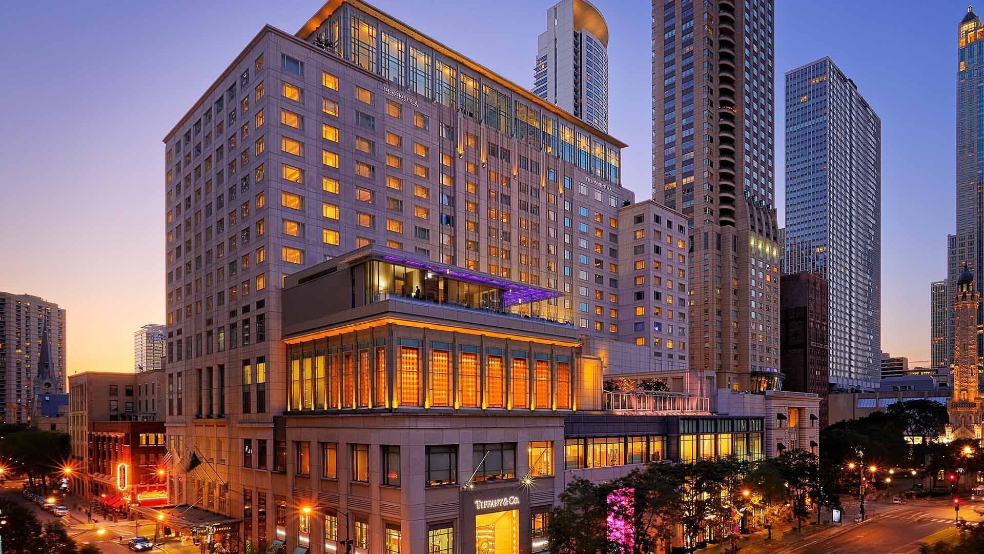 The Peninsula Chicago hotel exterior at dusk with city buildings and lights.