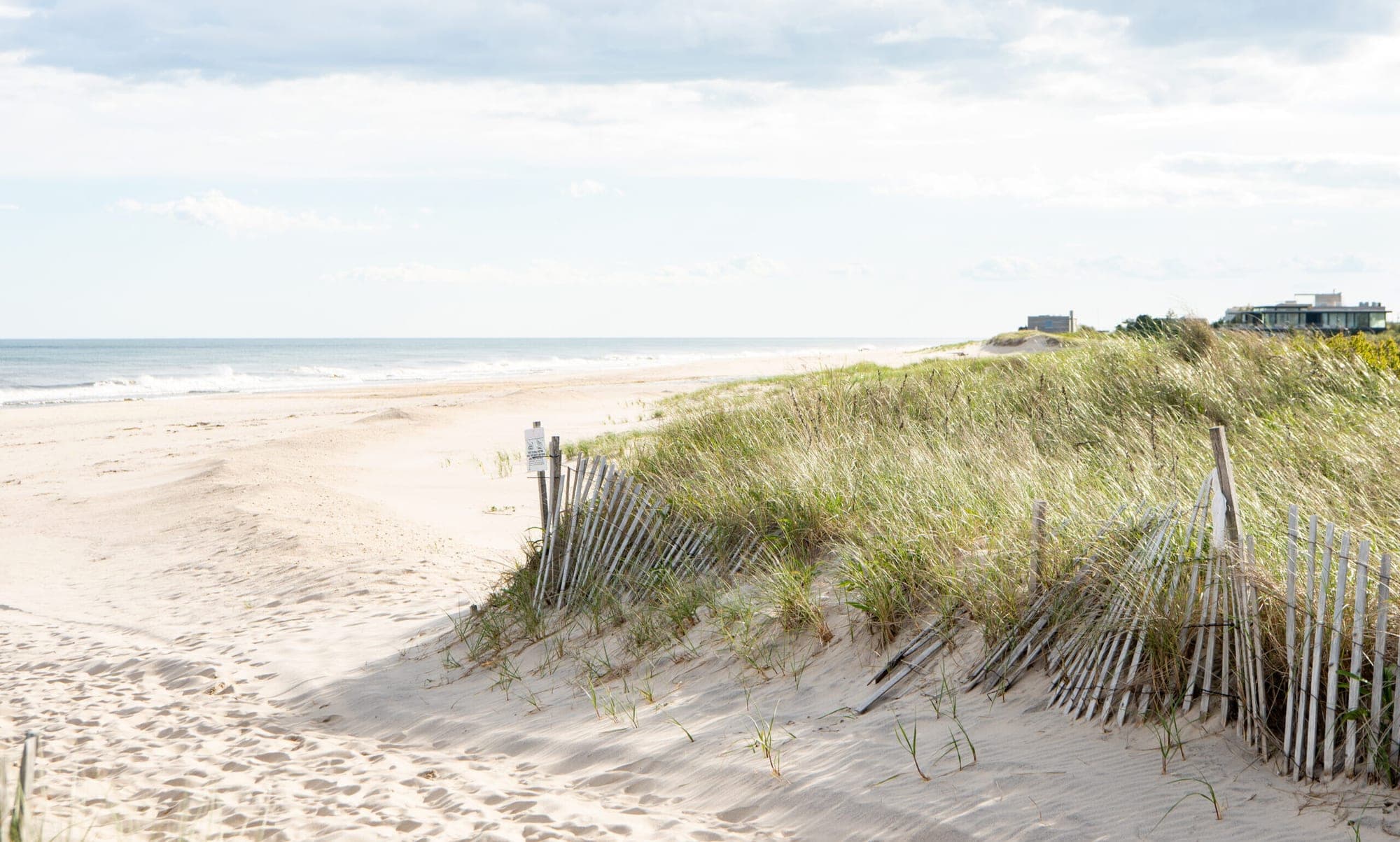 A sandy beach with dunes, sea, and distant buildings.
