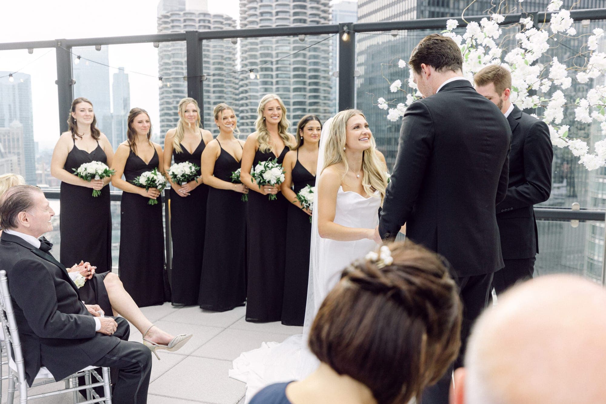 A wedding ceremony takes place on a rooftop terrace with a city skyline in the background.