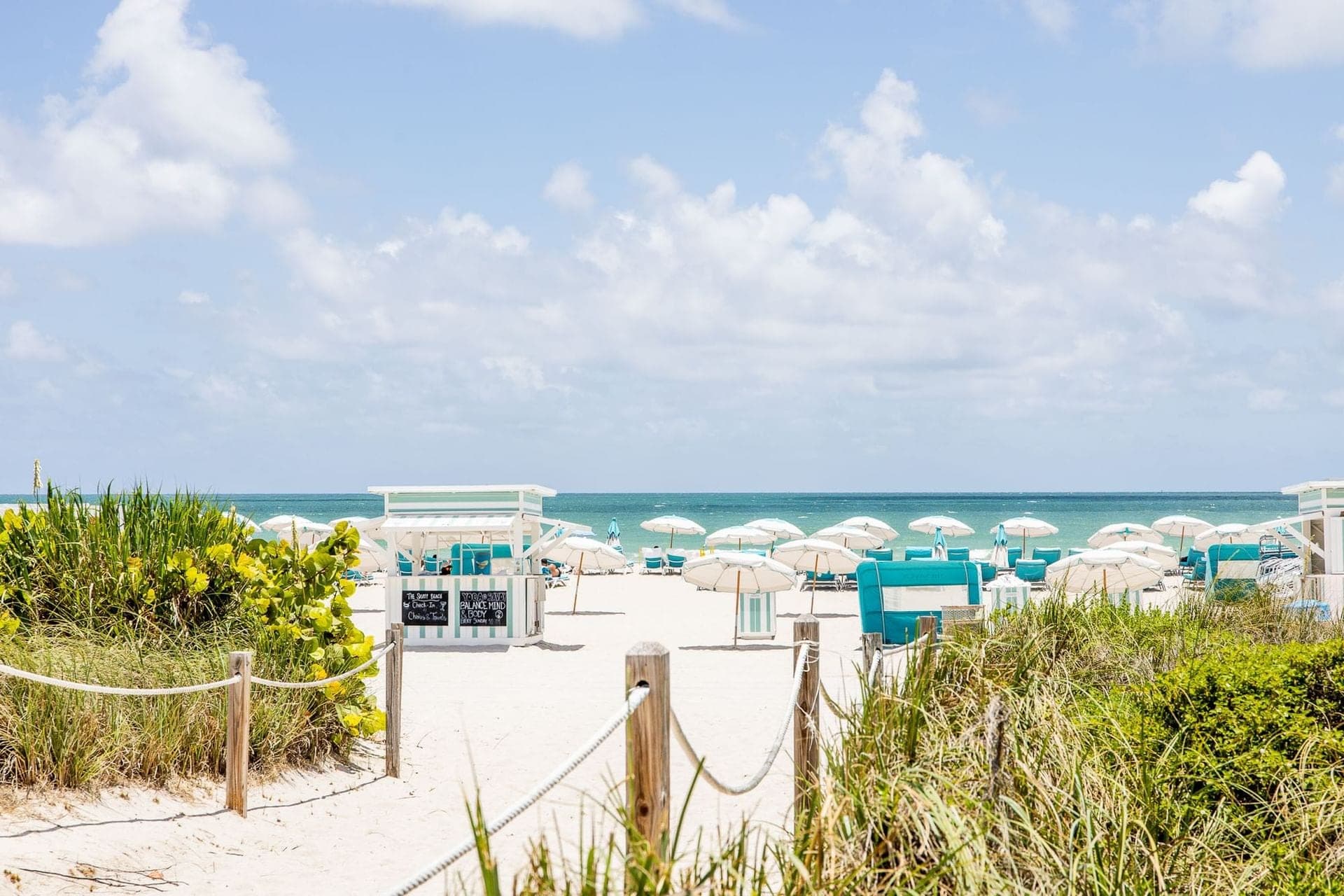 A beach with white umbrellas and teal cabanas facing the ocean.