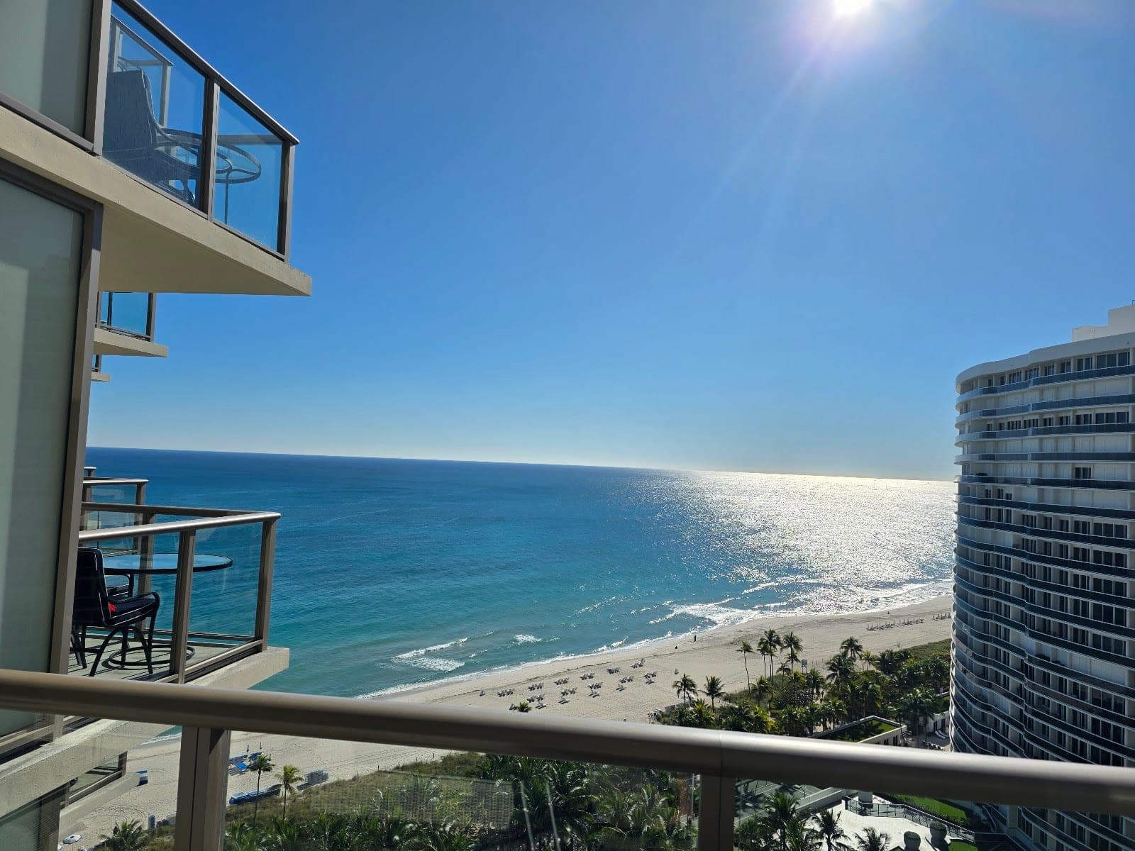 Balcony overlooking a beach and the ocean on a sunny day.