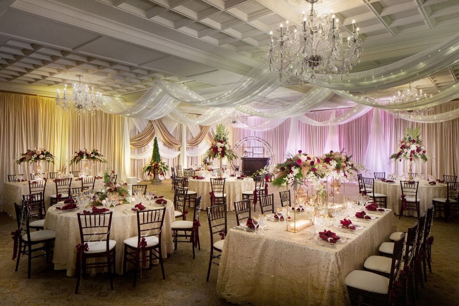 A wedding reception hall with round tables, chairs, and floral centerpieces.