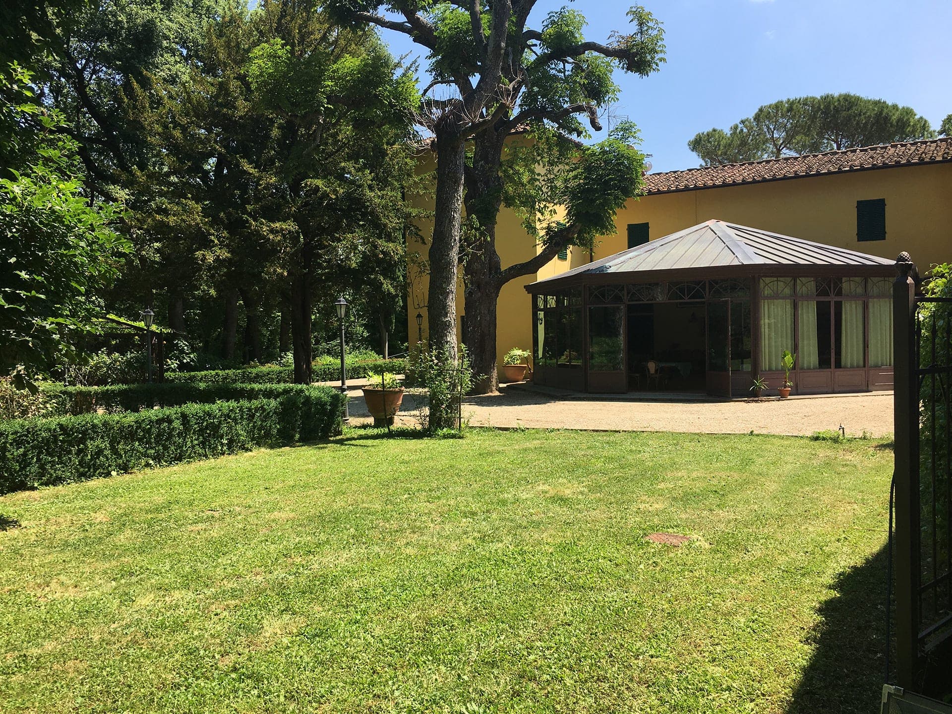 A conservatory with a glass roof and walls sits on a lawn with manicured hedges.