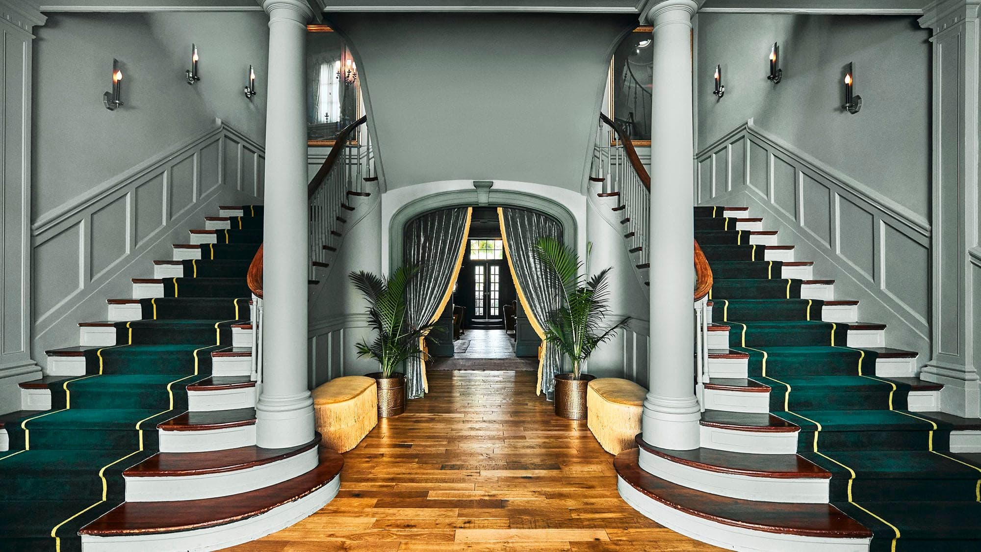 Grand staircase with green carpet and ornate banisters in a hotel foyer.