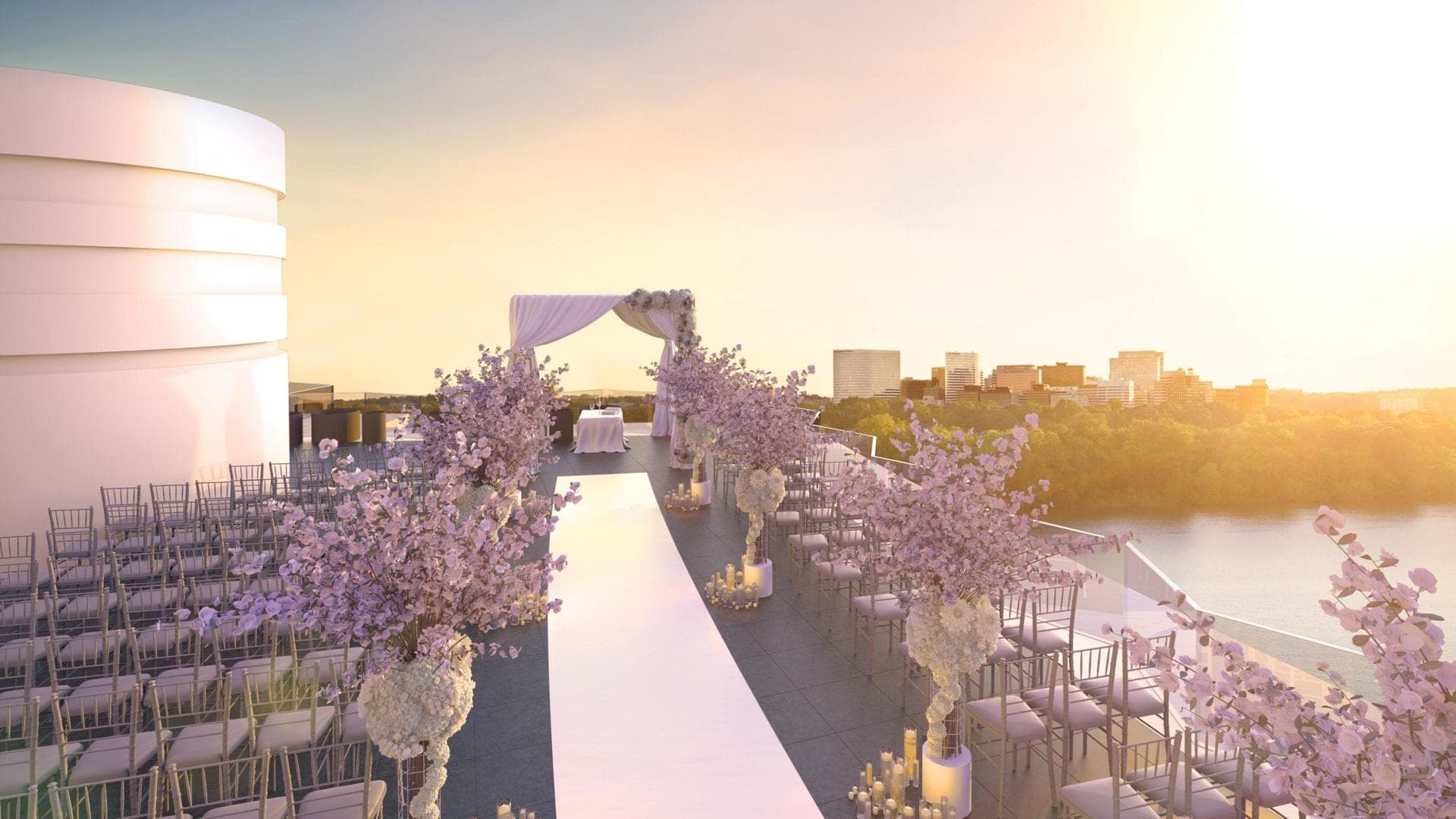 Rooftop wedding ceremony setup with chairs, aisle, and floral decorations overlooking a city and river at sunset.