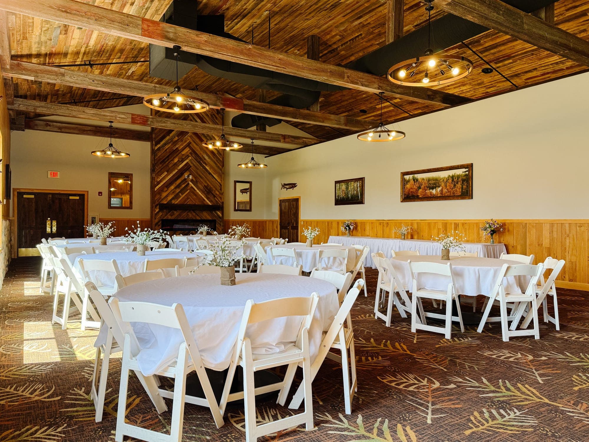 A wedding reception hall with round tables covered in white cloths and white chairs.